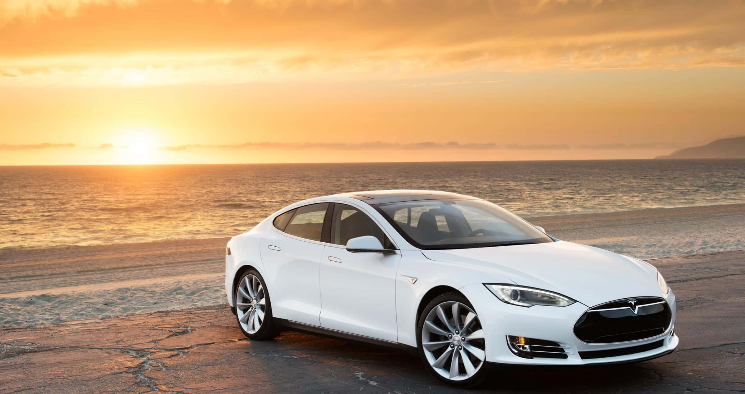特斯拉 桌布 壁紙 — 一架時尚的白色Tesla房車停泊在沙灘上，金色夕陽下海浪翻滾。