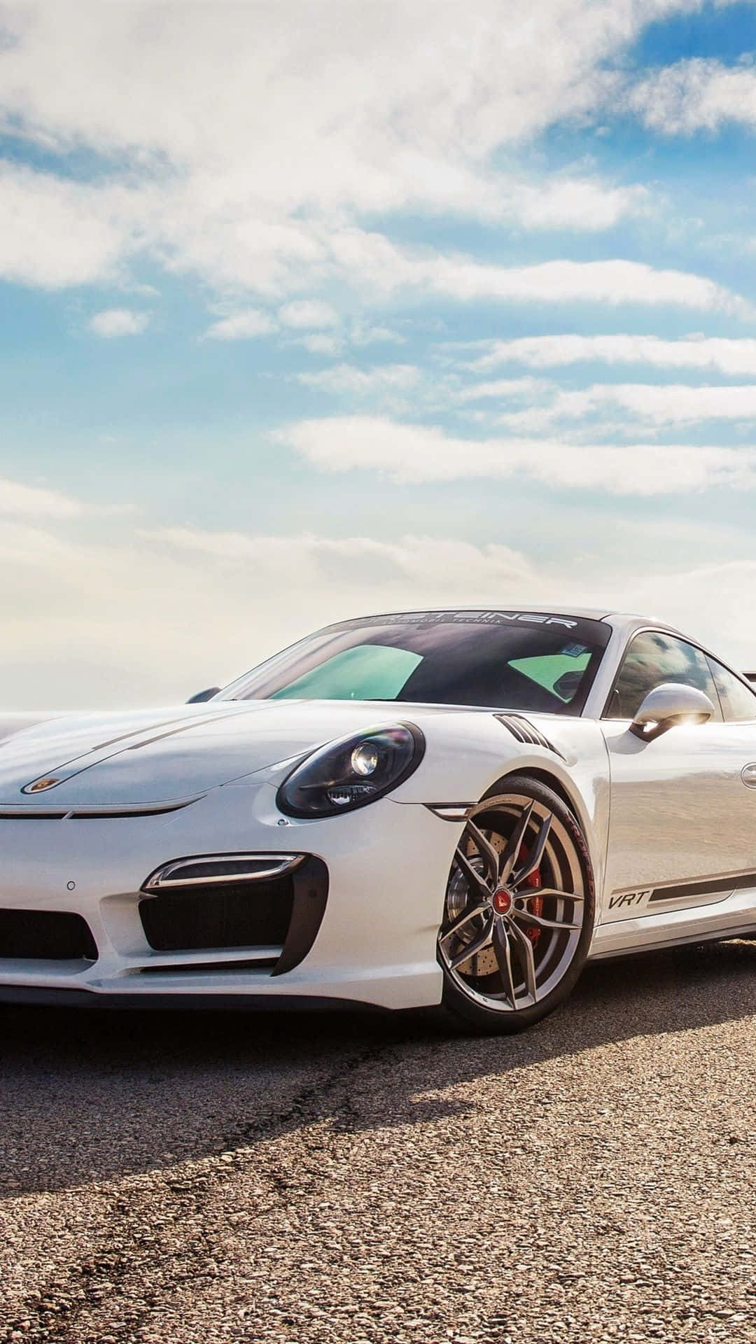 Porsche iPhone 桌布 壁紙 — 一架時尚的白色保時捷911 GT3 RS跑車停泊在碎石路上，天空湛藍，白雲點綴。