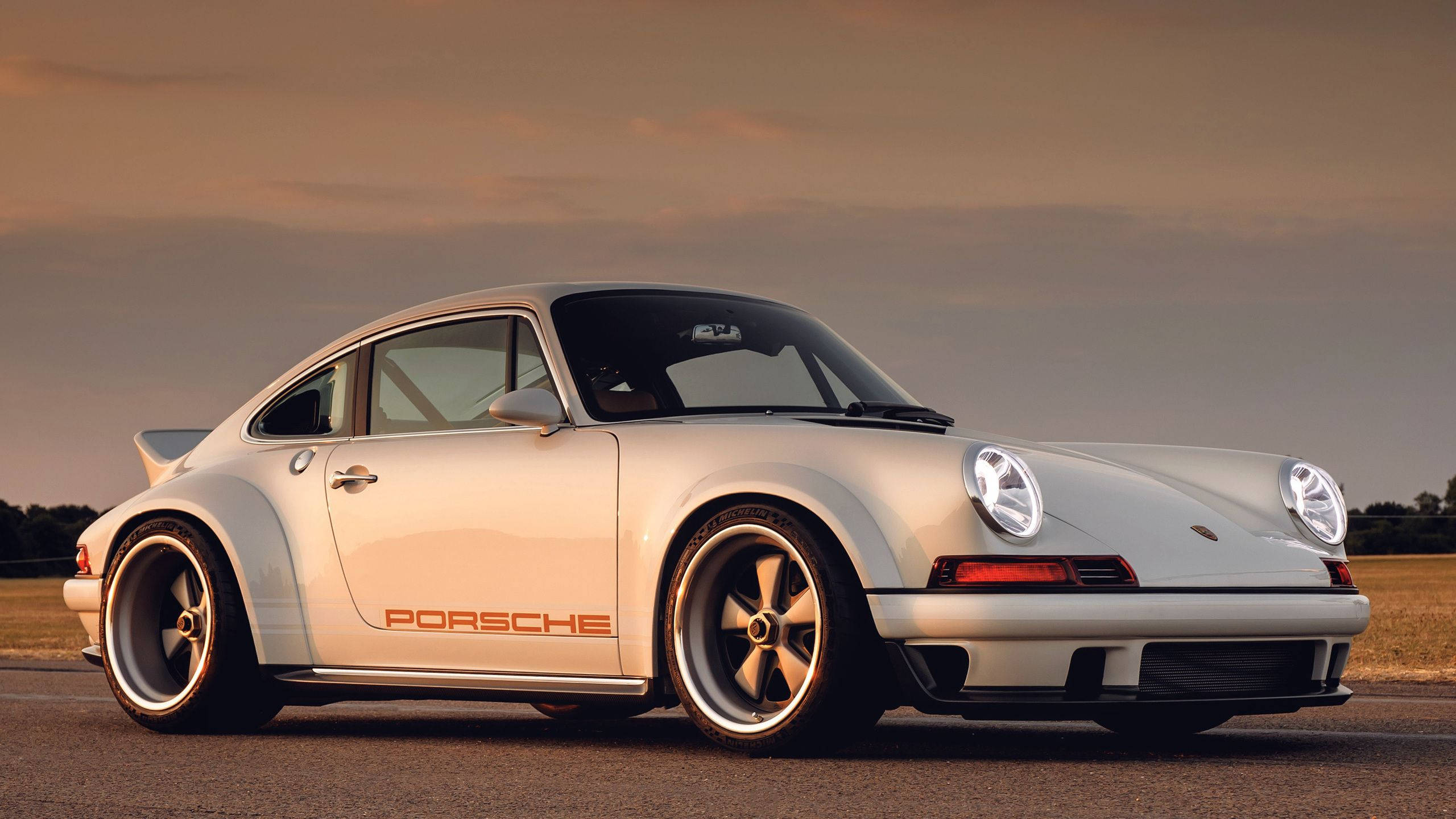 Singer 桌布 壁紙 — 一架時尚的白色保時捷911經典跑車停泊在瀝青路上，正值黃金時段，溫暖的夕陽照明。