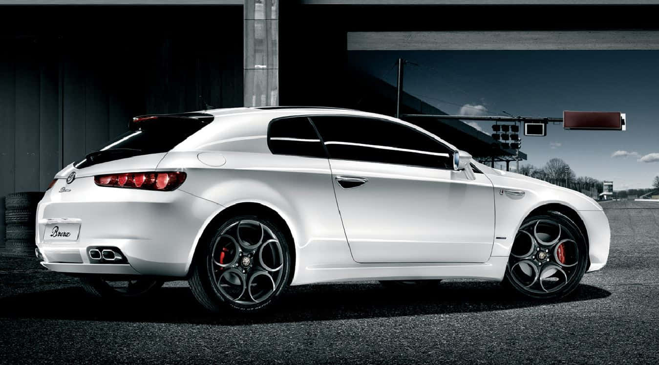 Alfa Romeo Brera 桌布 壁紙 — 一架時尚的白色愛快羅密歐Brera跑車停泊在瀝青賽道上，背景是戲劇性的天空和工業建築。