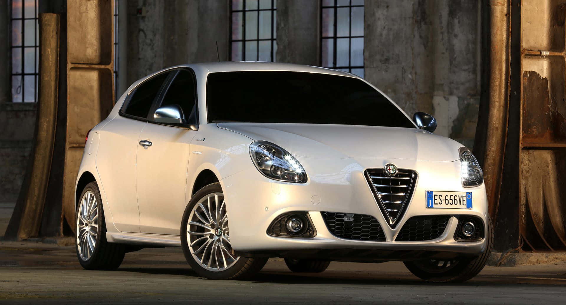 Alfa Romeo Giulietta 桌布 壁紙 — 一架時尚的白色愛快羅密歐Giulietta停放在溫暖燈光的鄉村工業環境中。