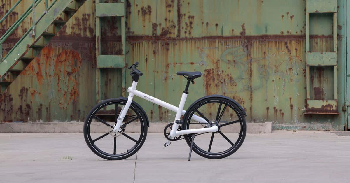 Electric Bike 桌布 壁紙 — 一架時尚的白色摺疊腳踏車，靠著一道帶樓梯的風化綠色鏽蝕金屬牆。