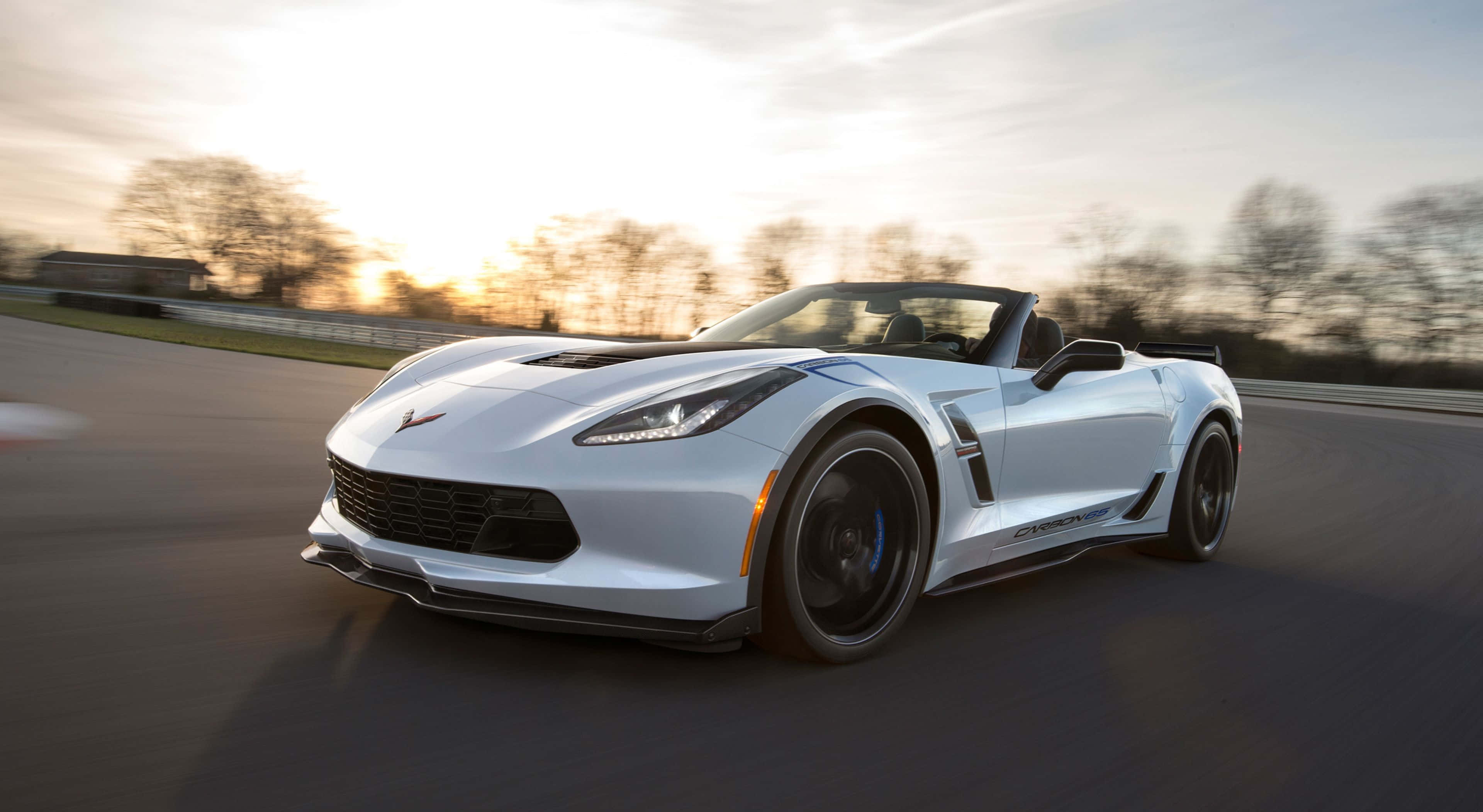 Chevrolet Corvette Grand Sport 桌布 壁紙 — 一架時尚的白色敞篷跑車在日落時分沿著賽道奔馳，背景是模糊的樹木。