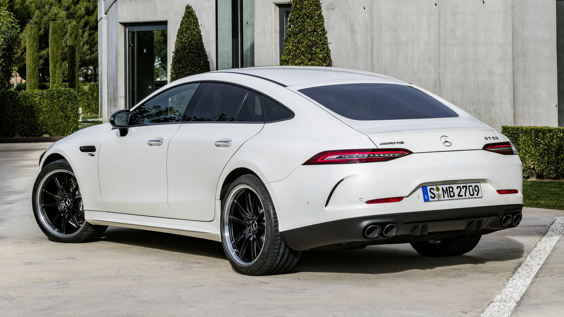 Mercedes Amg 桌布 壁紙 — 一架時尚的白色梅賽德斯-AMG GT 63 S 停放在混凝土車道上，旁邊是帶有修剪整齊樹籬的現代建築。