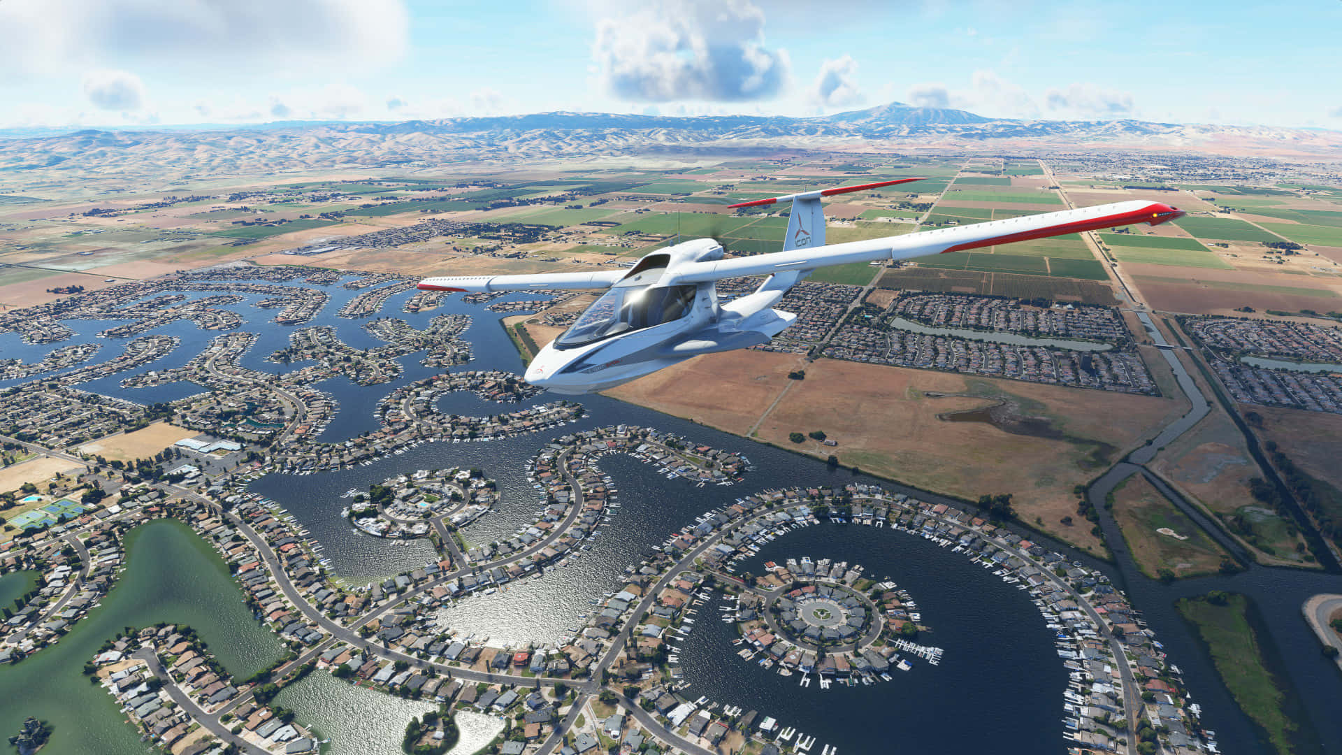 1080p Microsoft Flight Simulator 桌布 壁紙 — 一架時尚的白色水上飛機帶有紅色機翼，在明亮的藍天下低空飛過一個擁有蜿蜒運河和遊艇碼頭的廣闊海濱社區。