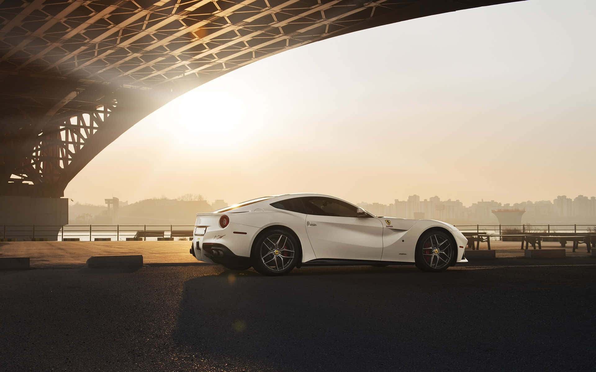 Ferrari F12 Berlinetta 桌布 壁紙 — 一架時尚的白色法拉利跑車停泊在橋下，金色晨曦照耀著城市海濱場景。