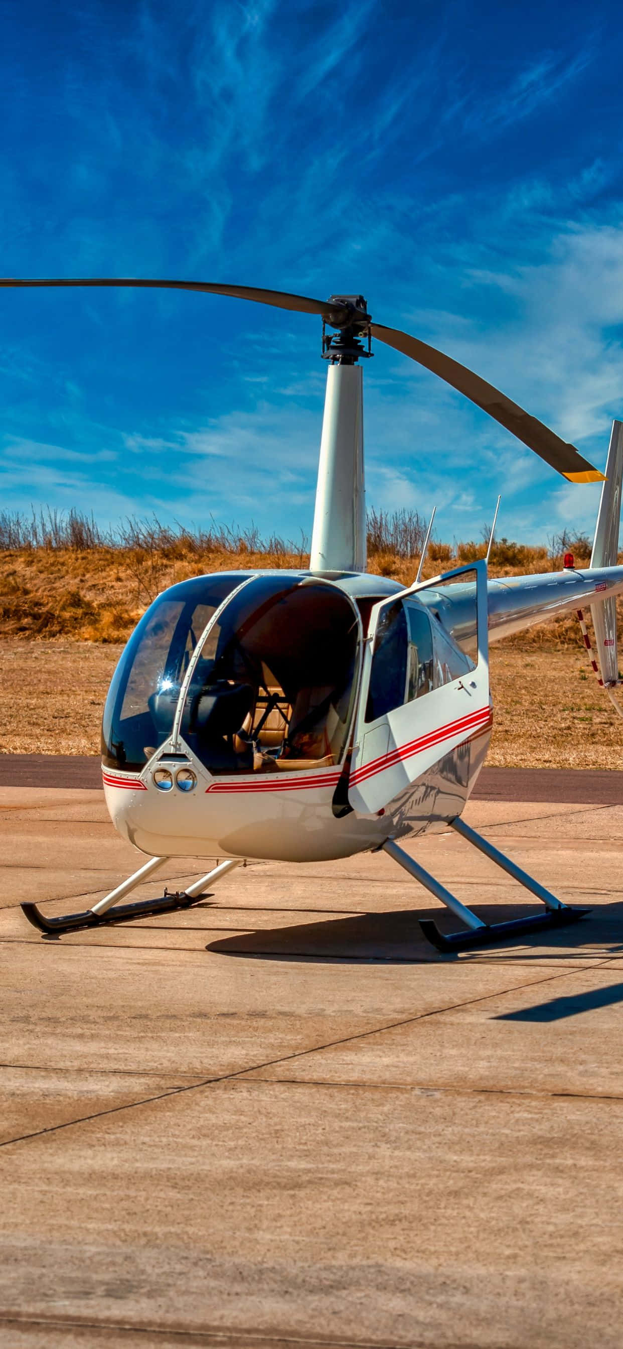 iPhone Xs Max Helicopters 桌布 壁紙 — 一架時尚的白色直升機帶有紅色條紋，停在混凝土平台上，上方是湛藍的天空和縷縷白雲。