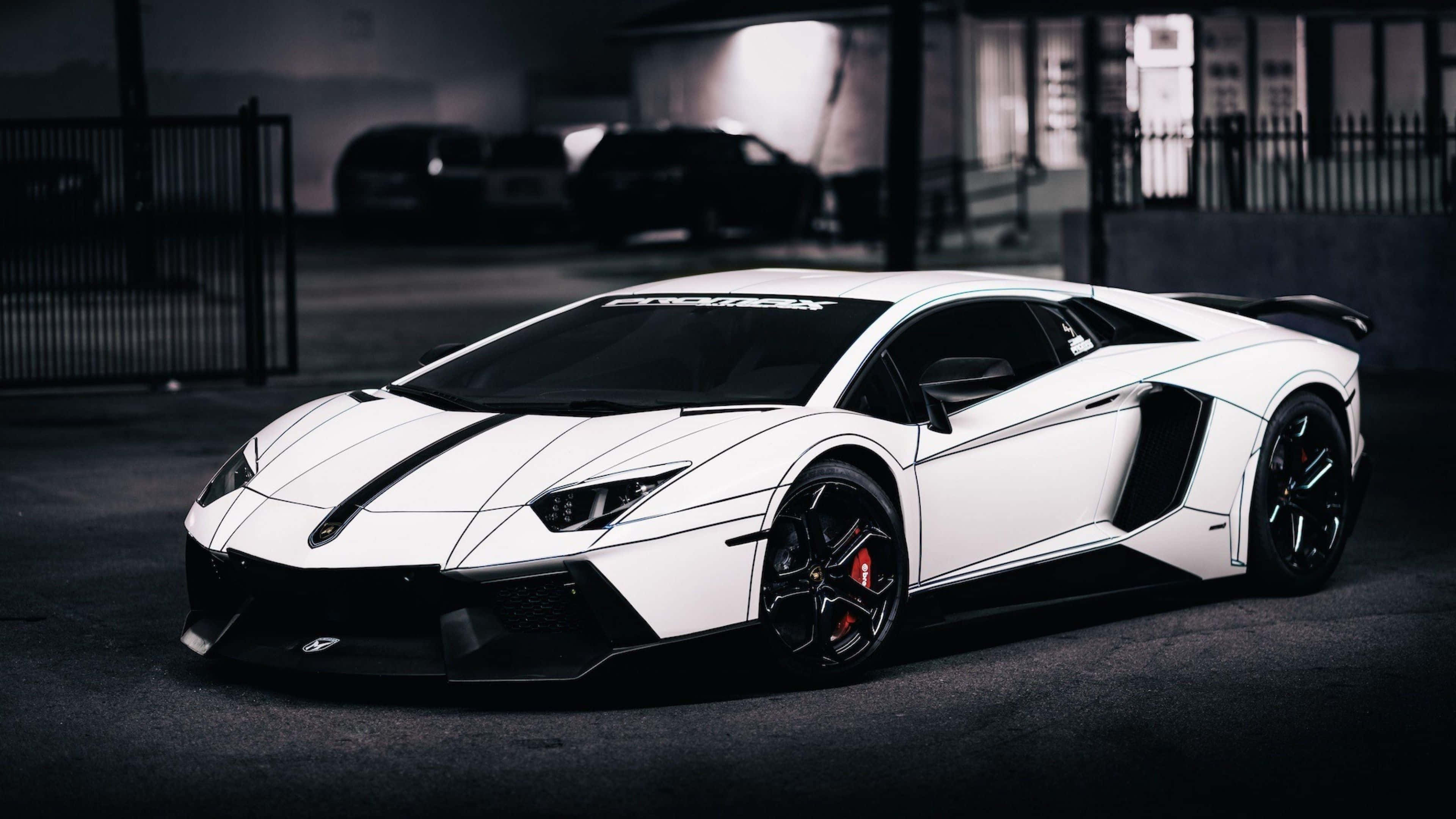 4K 藍寶堅尼 桌布 壁紙 — 一架時尚的白色藍寶堅尼Aventador，帶有黑色飾邊和紅色制動卡鉗，停泊在燈光昏暗的城市車庫中。