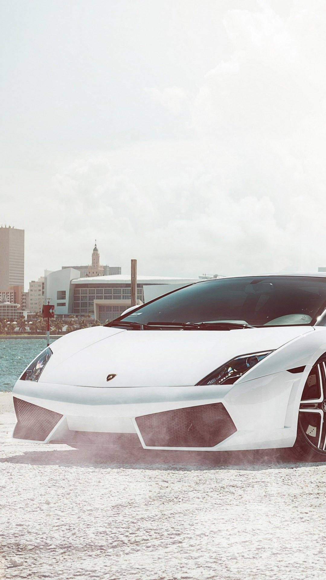 Cool Car 桌布 壁紙 — 一架時尚的白色藍寶堅尼在淺水中飄移，背景是朦朧的現代城市天際線。