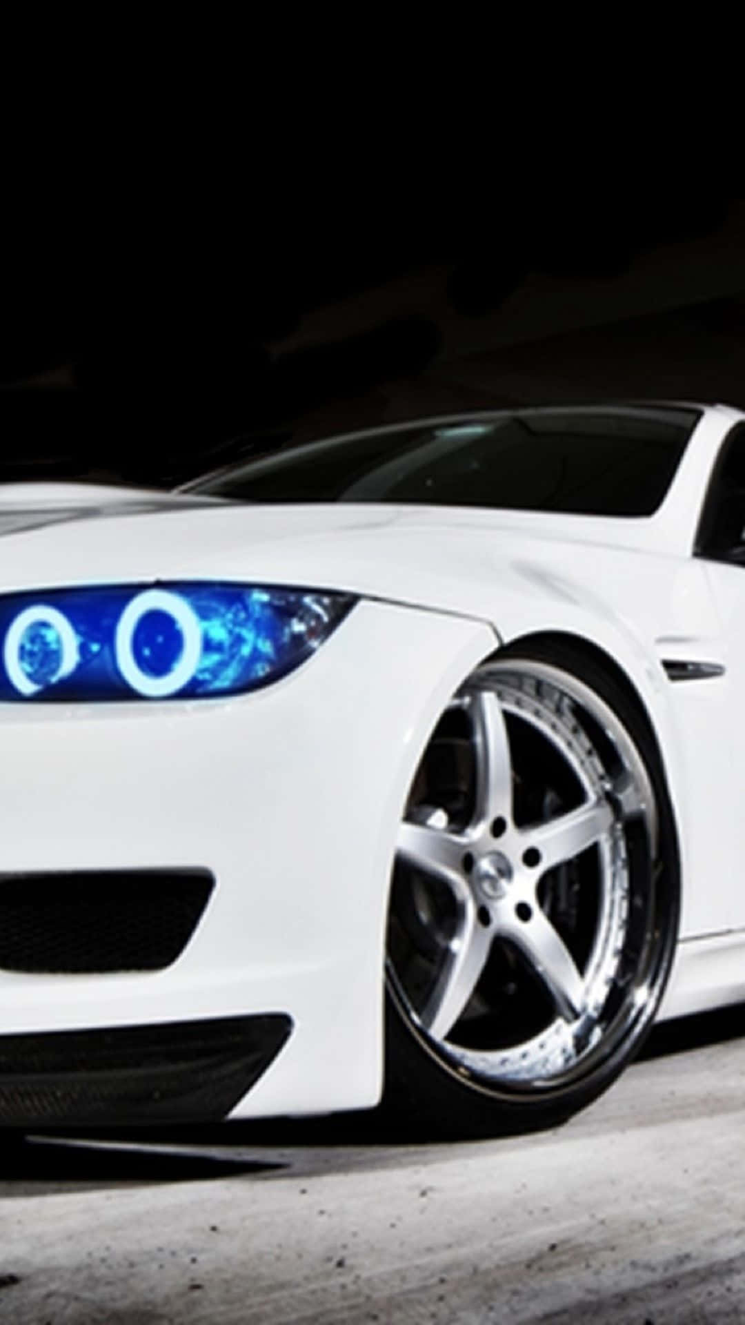 Bmw iPhone 桌布 壁紙 — 一架時尚的白色跑車，配備發光的藍色光環頭燈和定制鍍鉻輪圈，停在黑暗的車庫中。