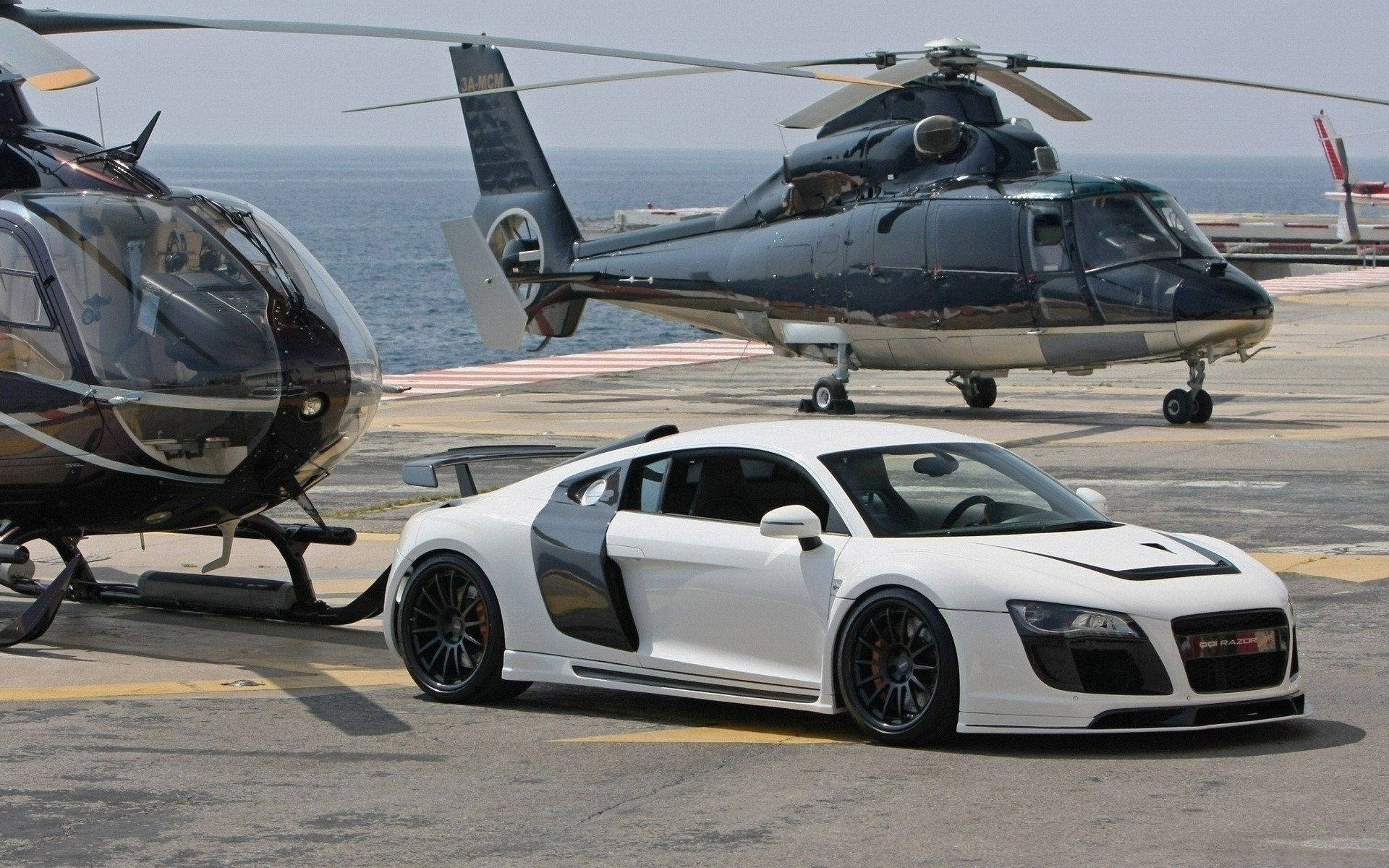 Helicopter 桌布 壁紙 — 一架時尚的白色跑車停在停機坪上，旁邊有兩架黑色直升機，背景是海洋。