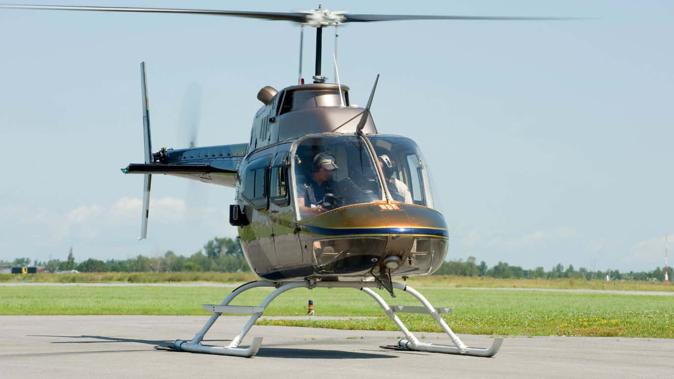 1366x768 Helicopters 桌布 壁紙 — 一架時尚的直升機帶有金色和藍色點綴，停在停機坪上，背景是晴朗的藍天和綠草。