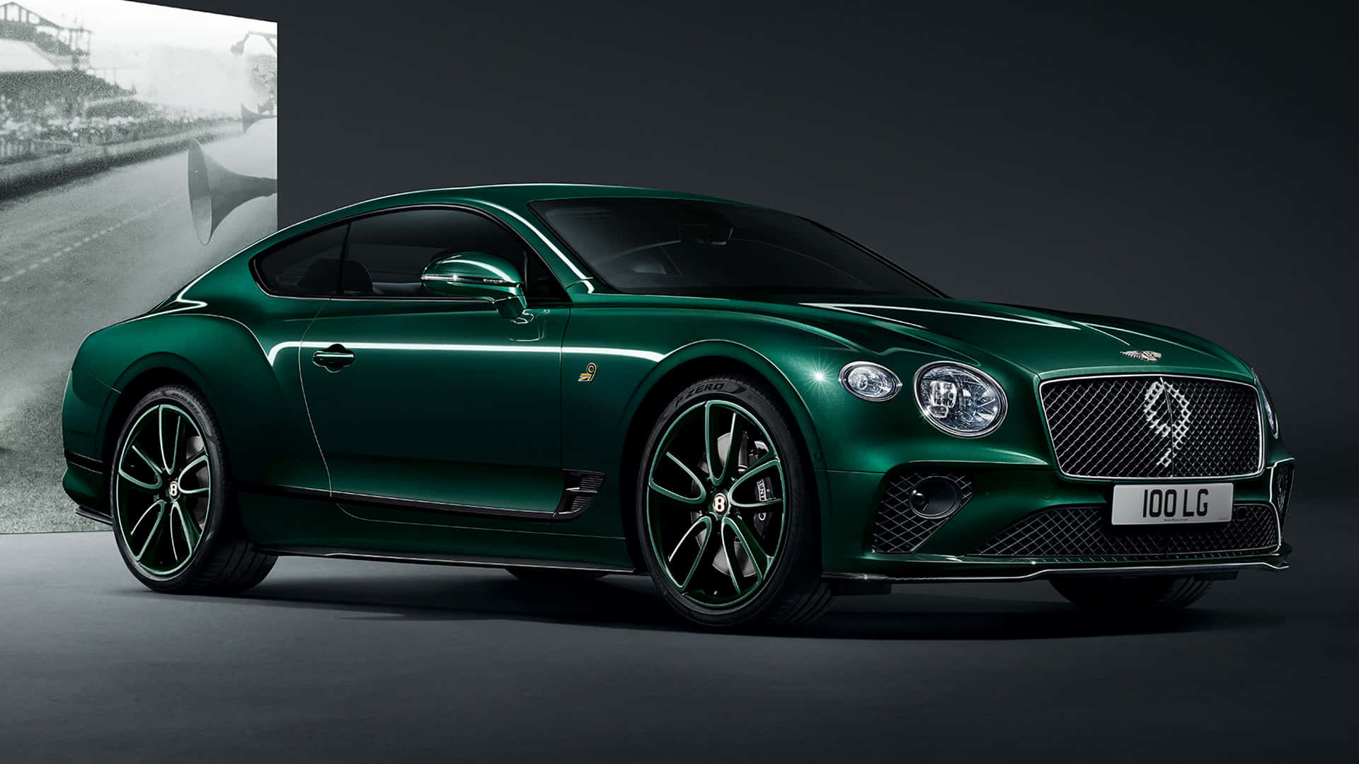 桌布 壁紙 — 一架時尚的祖母綠色賓利 Continental GT 雙門轎跑車，在攝影棚燈光下，以一張復古賽車照片為背景，閃閃發光。
