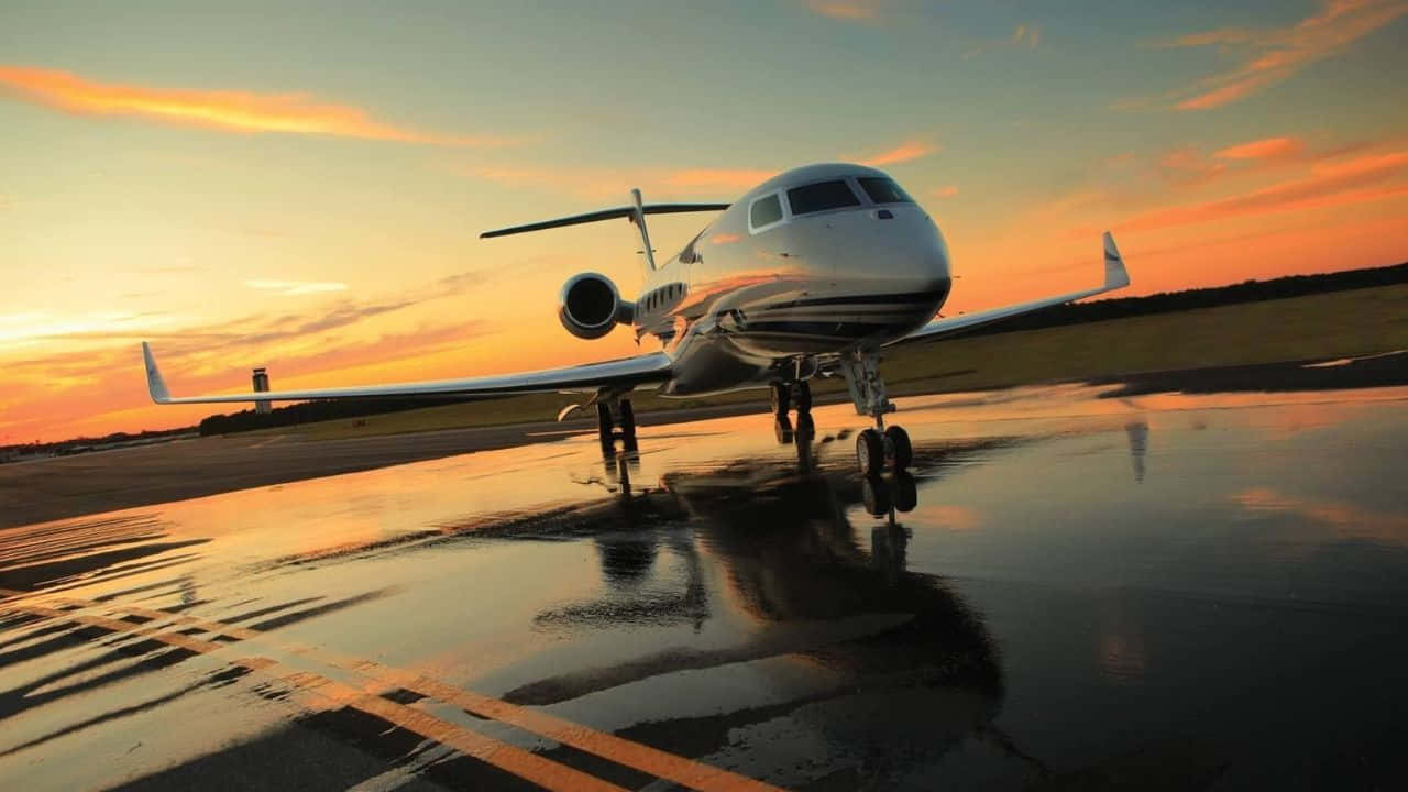 720p Plane 桌布 壁紙 — 一架時尚的私人飛機停在潮濕的跑道上，反射出熾熱的日落色調，映照在停機坪上。