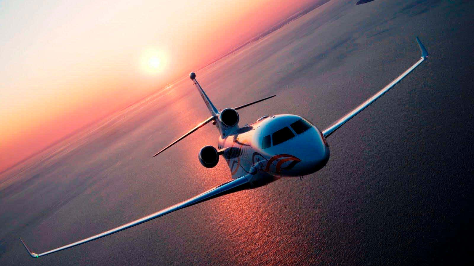 HD Plane 桌布 壁紙 — 一架時尚的私人飛機在廣闊的海洋上空翱翔，夕陽西下，火紅的橙色和粉紅色天空倒映在水面上。