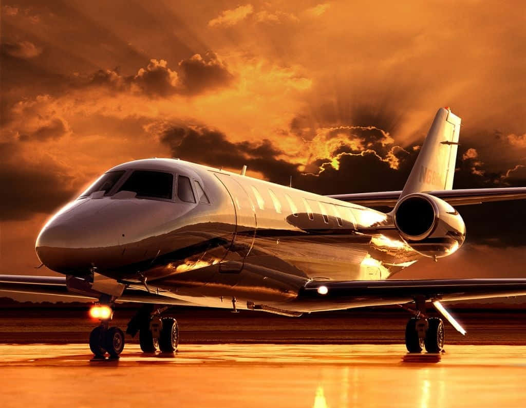 Jet 桌布 壁紙 — 一架時尚的私人飛機在戲劇性的金色日落和燦爛雲彩下在跑道上閃閃發光。