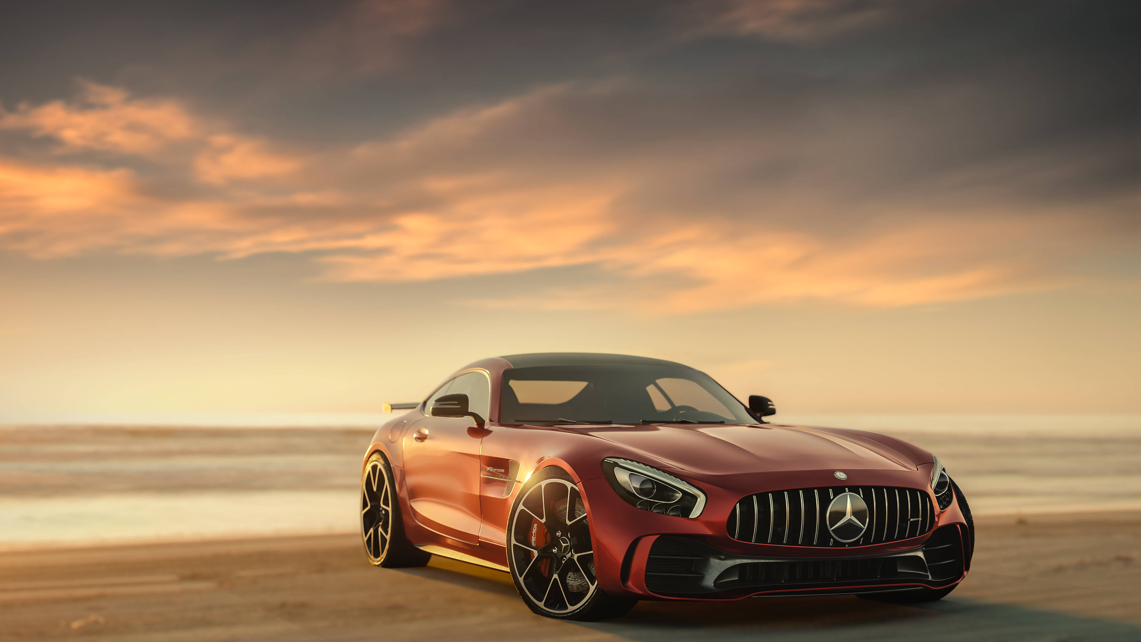 Amg 桌布 壁紙 — 一架時尚的紅色 Mercedes-AMG GT 跑車停泊在日落時分的沙灘上，上方有金色雲彩。