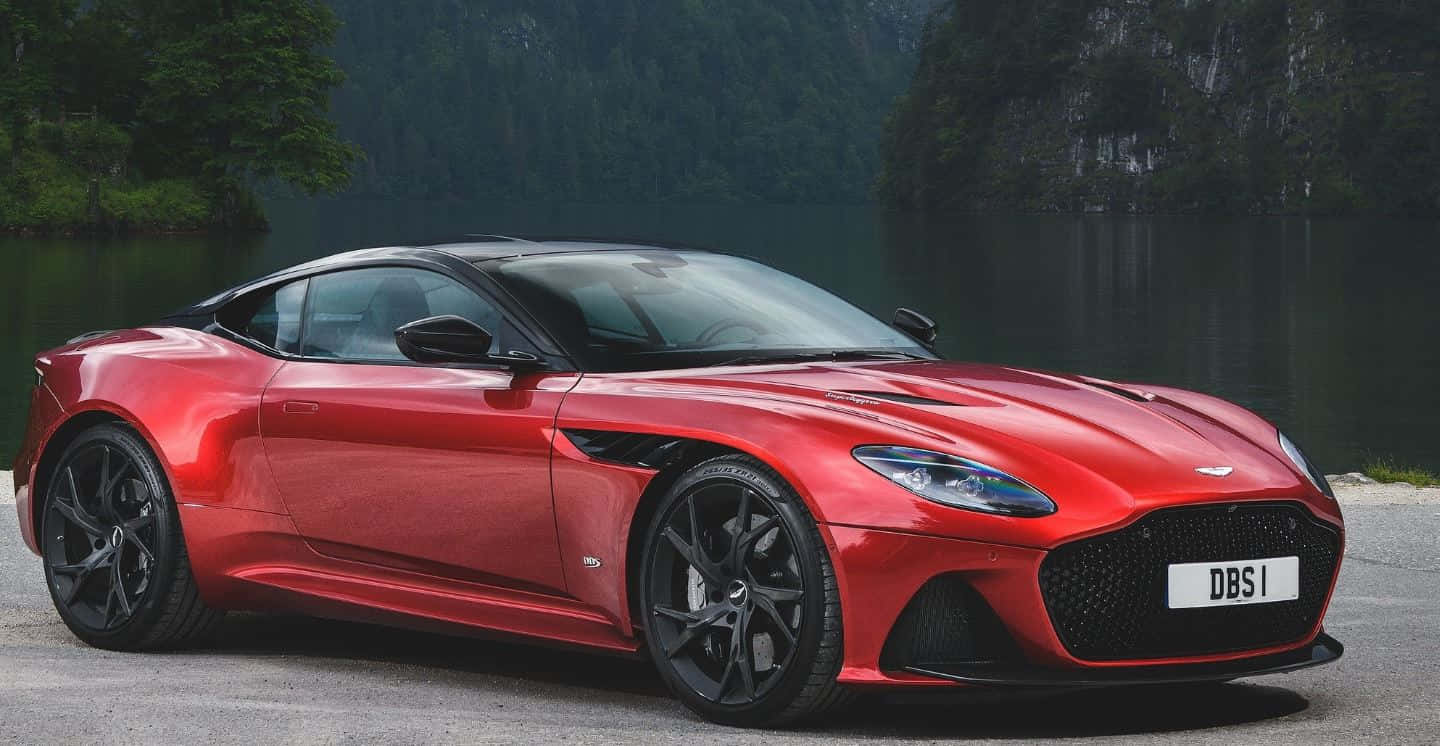 Aston Martin Dbs Superleggera 桌布 壁紙 — 一架時尚的紅色Aston Martin DBS1跑車停泊在平靜的湖邊，周圍是森林覆蓋的山丘。