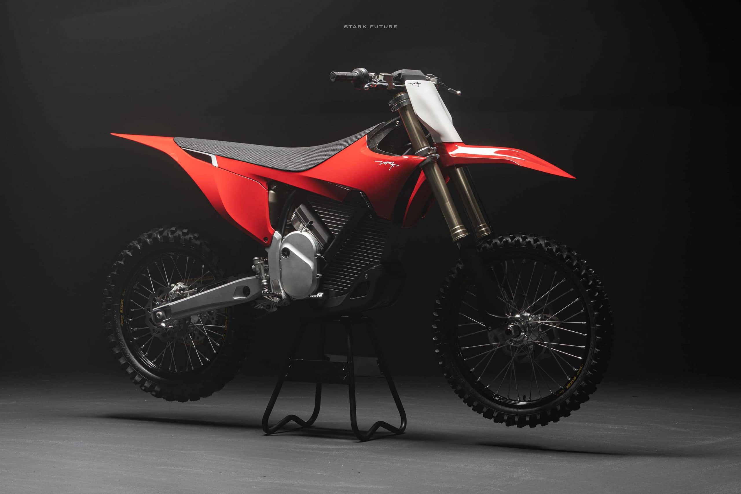 Dirtbike 桌布 壁紙 — 一架時尚的紅色和黑色越野摩托車在戲劇性燈光下，立於深色工作室背景前的支架上。