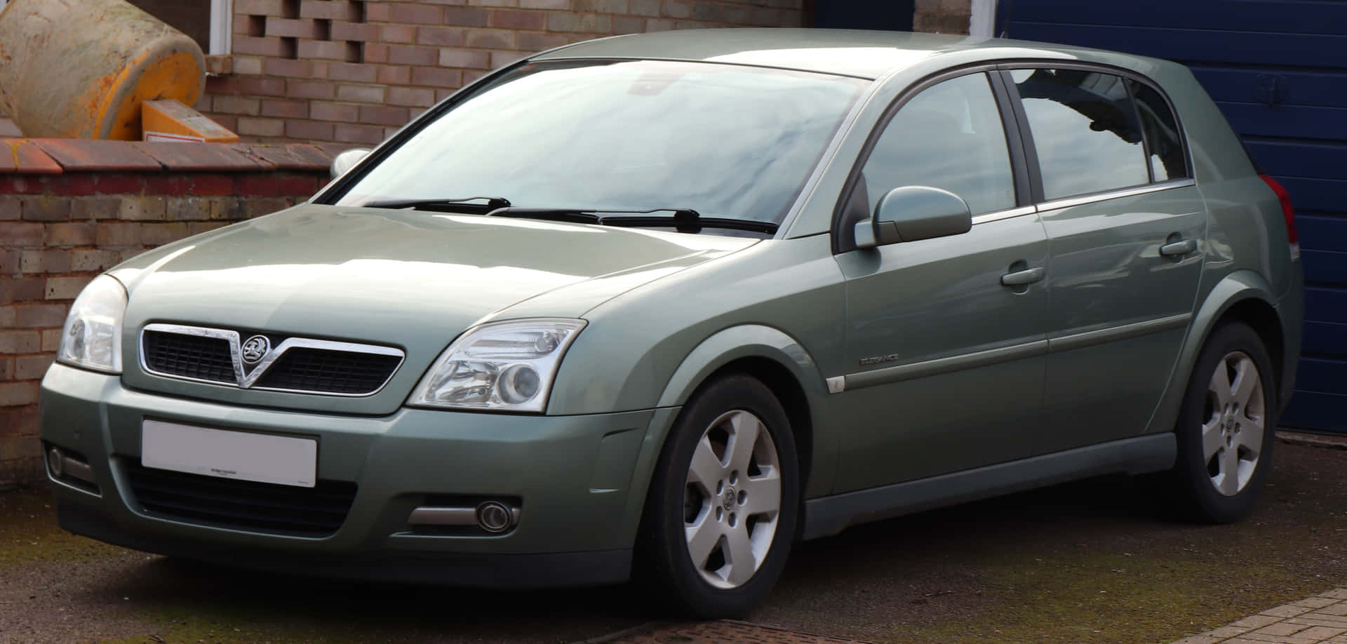  壁紙 — 一架時尚的綠色Vauxhall Vectra掀背車停放在鋪砌的車道上，旁邊是磚牆和藍色車庫門。