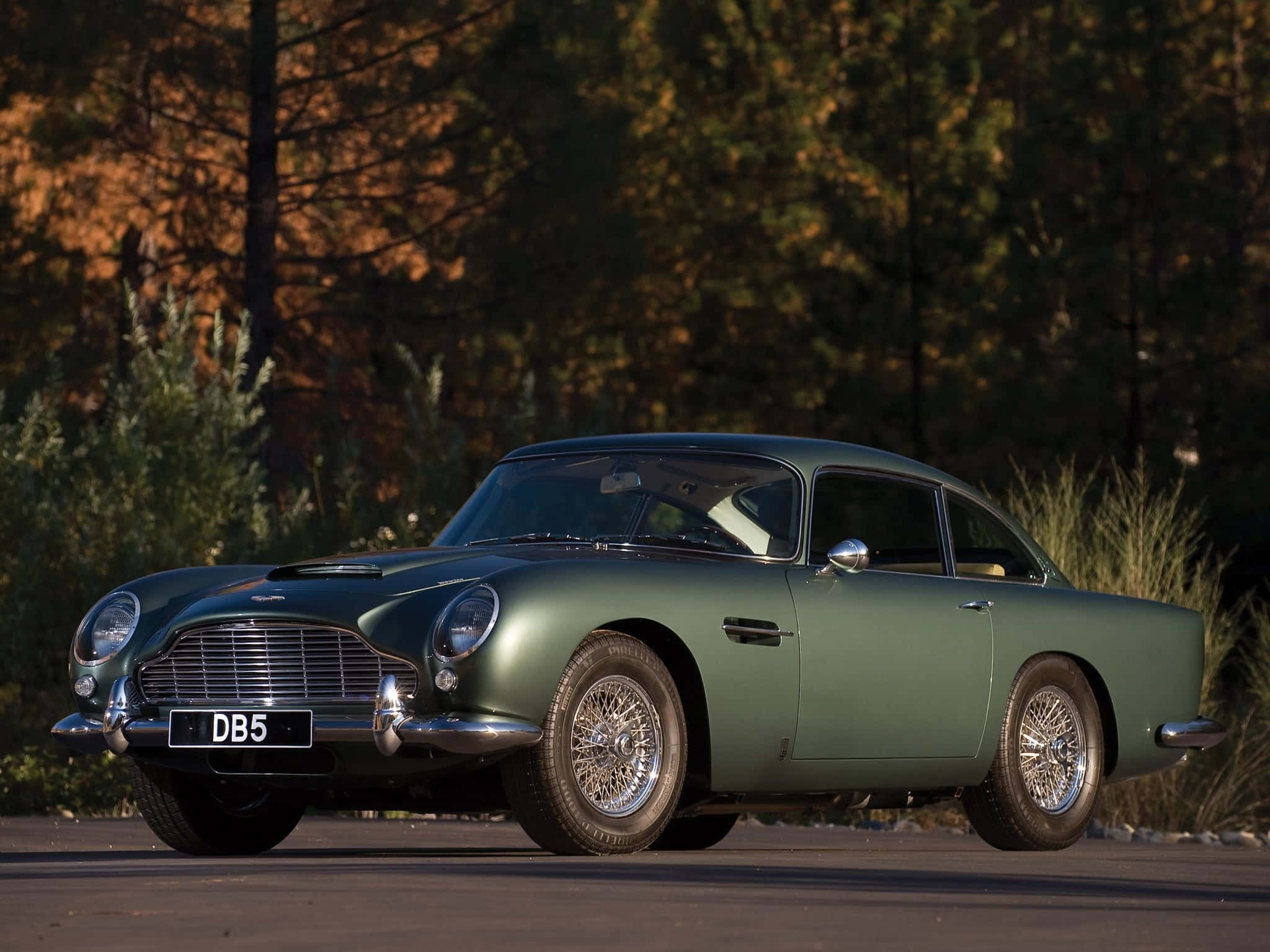 Aston Martin Db5 桌布 壁紙 — 一架時尚的綠色經典 Aston Martin DB5 停泊在人行道上，樹木在溫暖的日落光芒中閃耀。