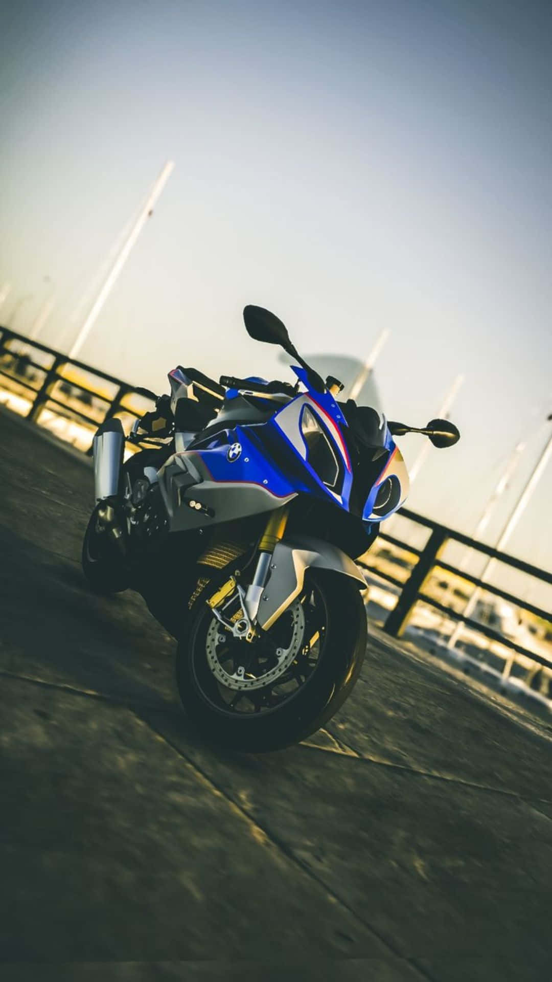 Superbike 桌布 壁紙 — 一架時尚的藍白色運動機車停泊在碼頭上，正值黃金時段，背景有模糊的船隻。