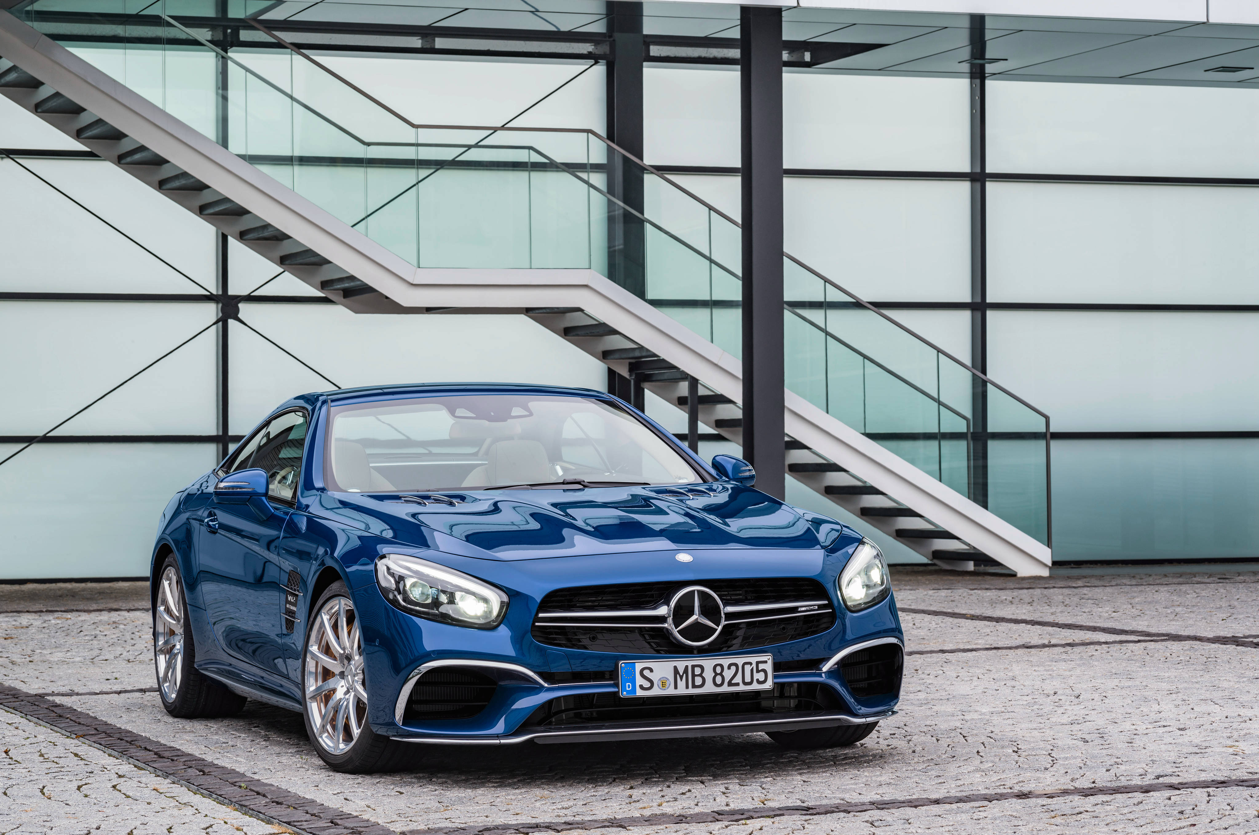 benz 4K 桌布 壁紙 — 一架時尚的藍色 Mercedes-AMG SL63 跑車停放在現代玻璃及鋼結構建築物前，建築物設有樓梯。