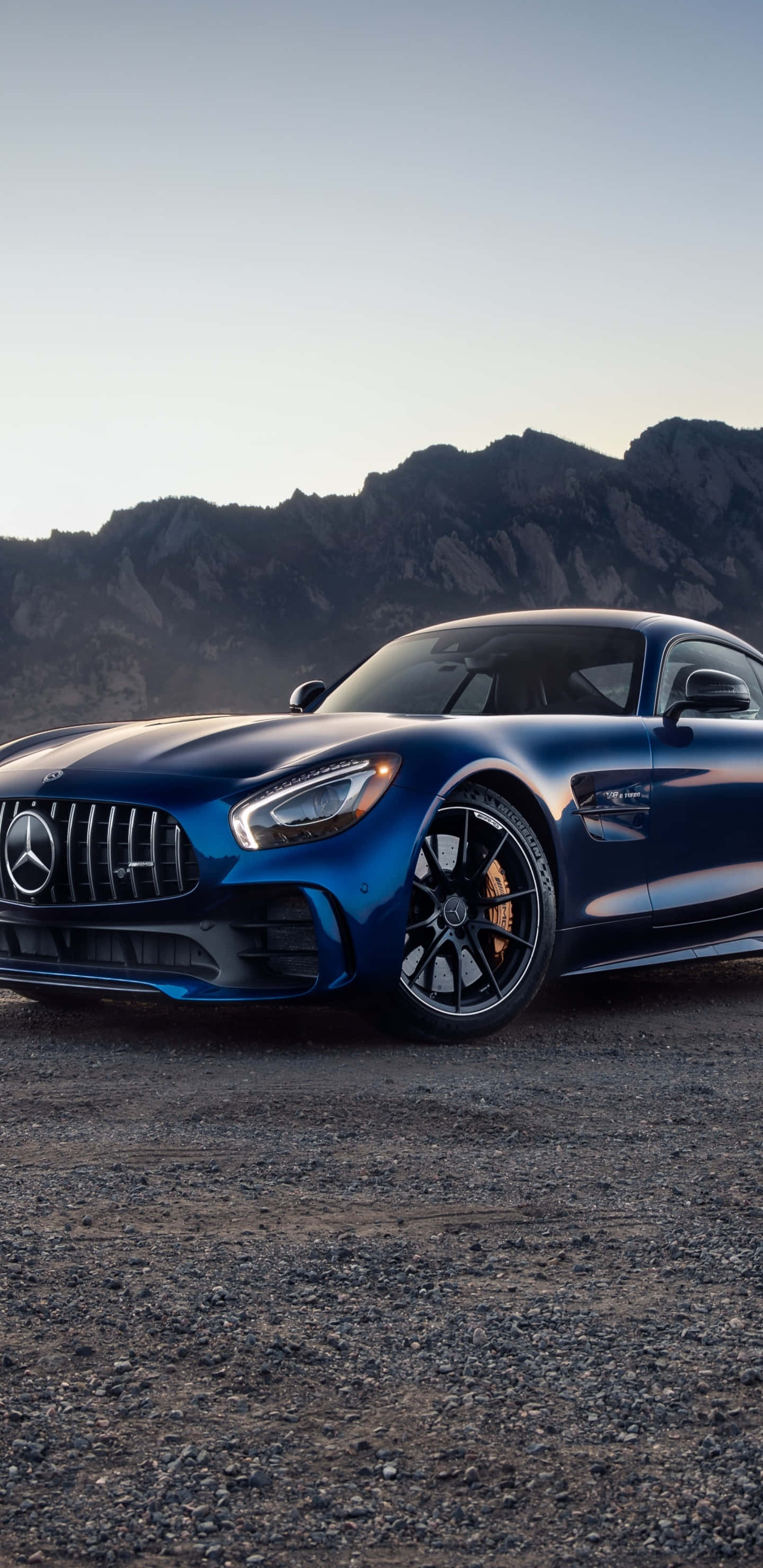 Blue Car 桌布 壁紙 — 一架時尚的藍色 Mercedes-AMG GT 跑車停在碎石上，背景是黃昏時崎嶇的山脈。