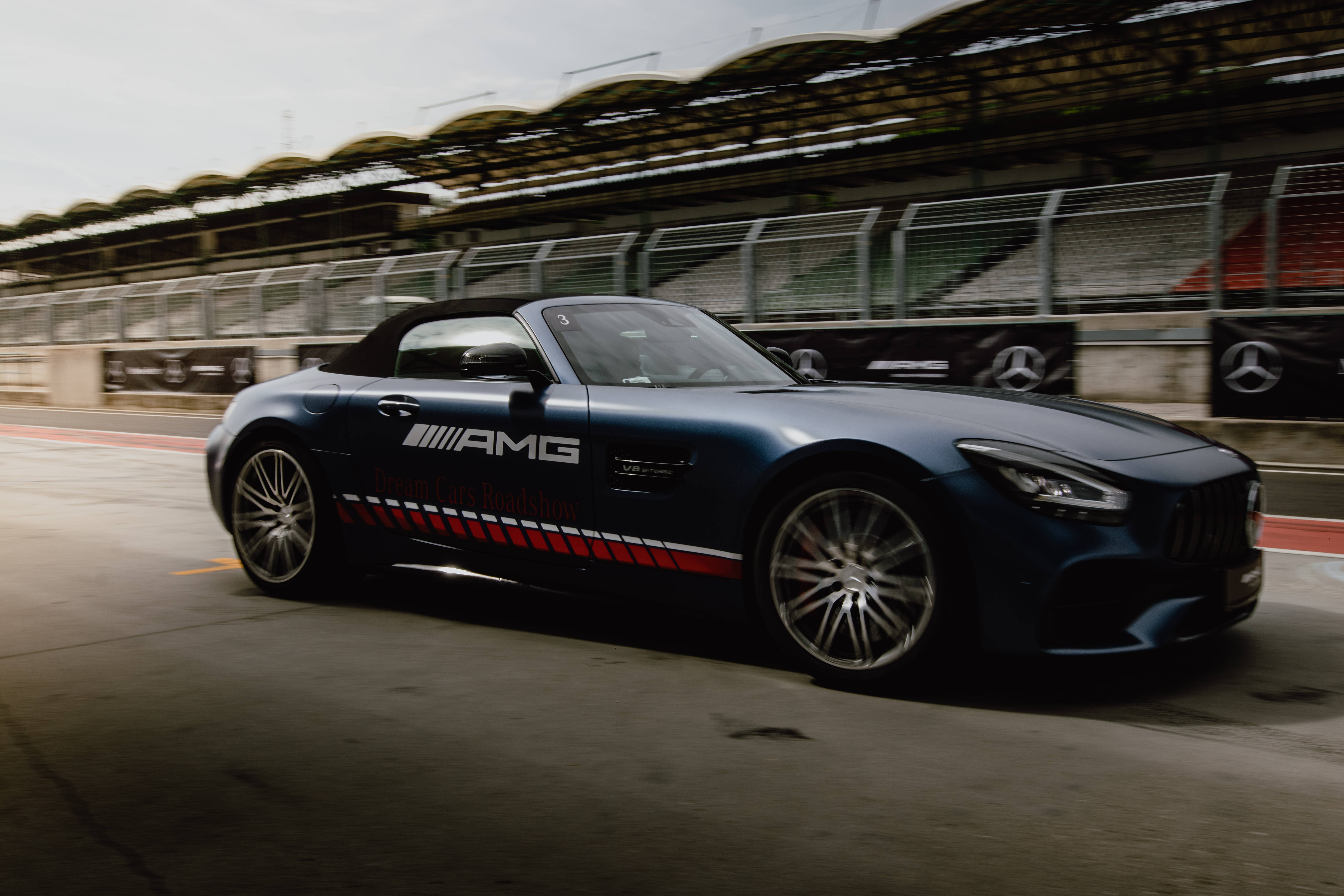 AMG iPhone 桌布 壁紙 — 一架時尚的藍色AMG跑車在賽道上疾馳，背景有動態模糊和看台座位。