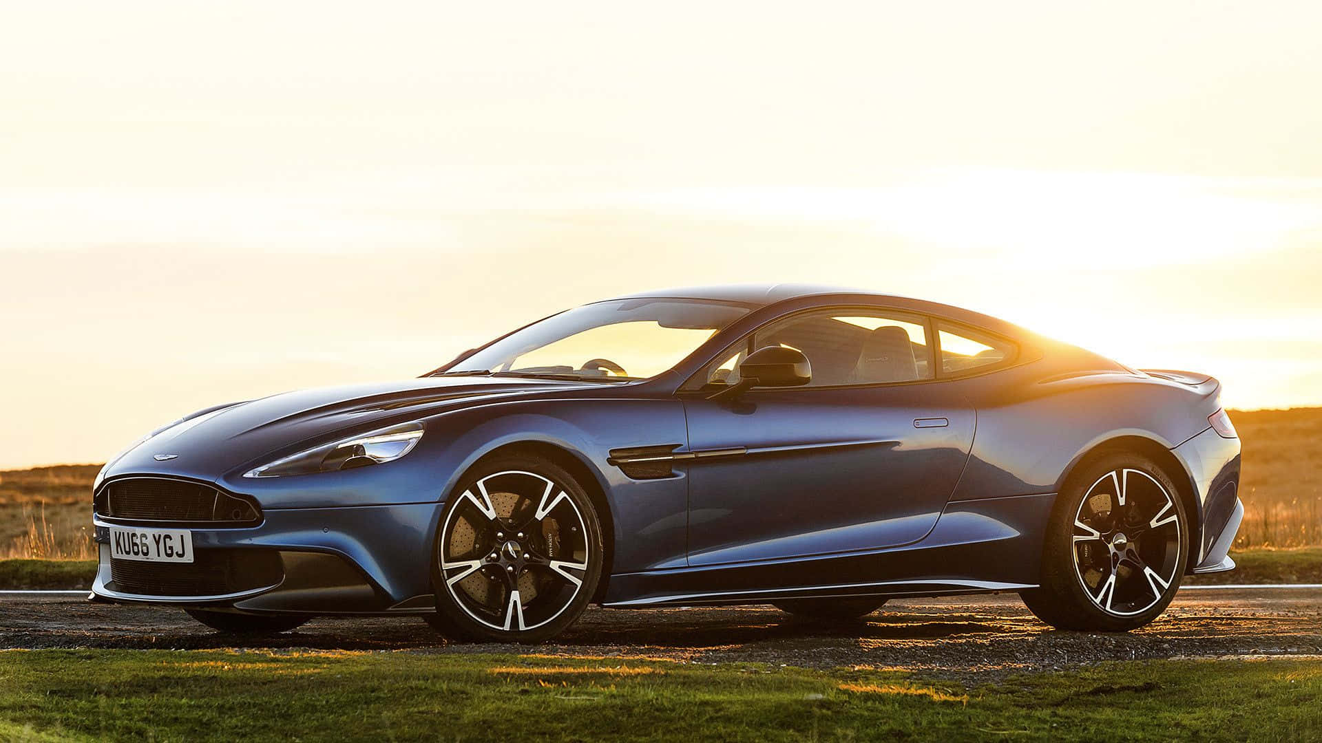 Aston Martin Vanquish 桌布 壁紙 — 一架時尚的藍色Aston Martin跑車在金色夕陽下駛過草地，溫暖的光線突顯其曲線。