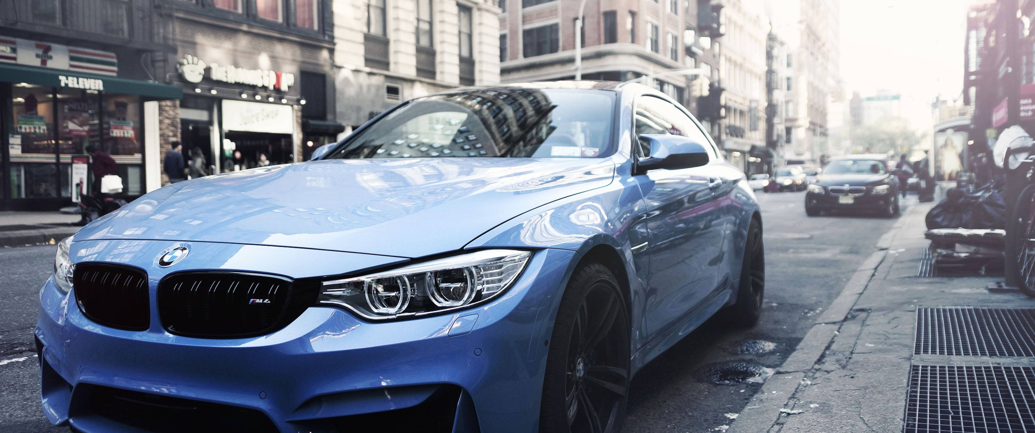 Bmw Cars 桌布 壁紙 — 一架時尚的藍色BMW M4雙門跑車停在繁華的城市街道上，引擎蓋上反射著光澤。