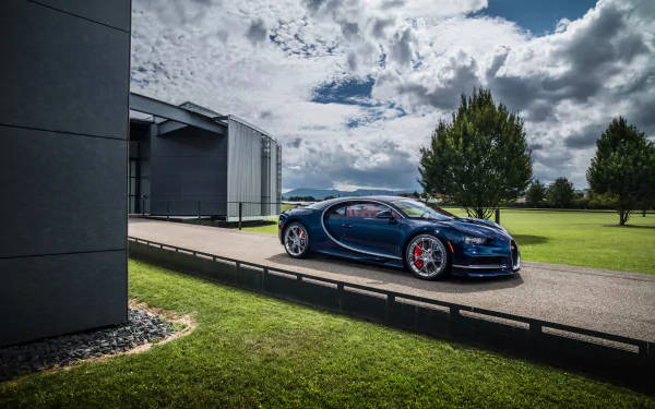 藍色Bugatti跑車停放在現代建築和綠色草坪附近，天空多雲。 — 4K 壁紙