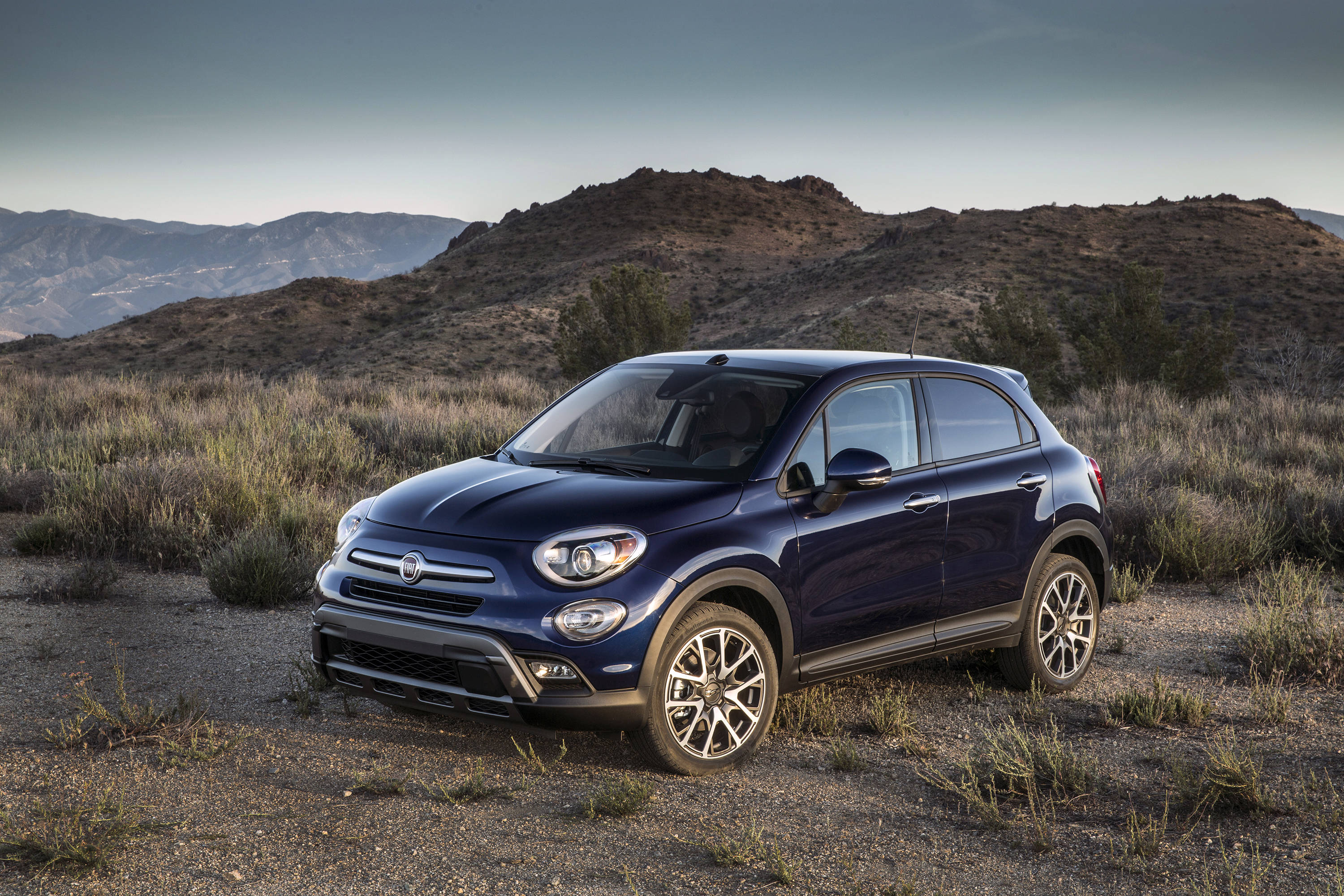Fiat 桌布 壁紙 — 一架時尚的藍色Fiat 500X SUV停在乾燥丘陵景觀的碎石上，天空柔和暮色。