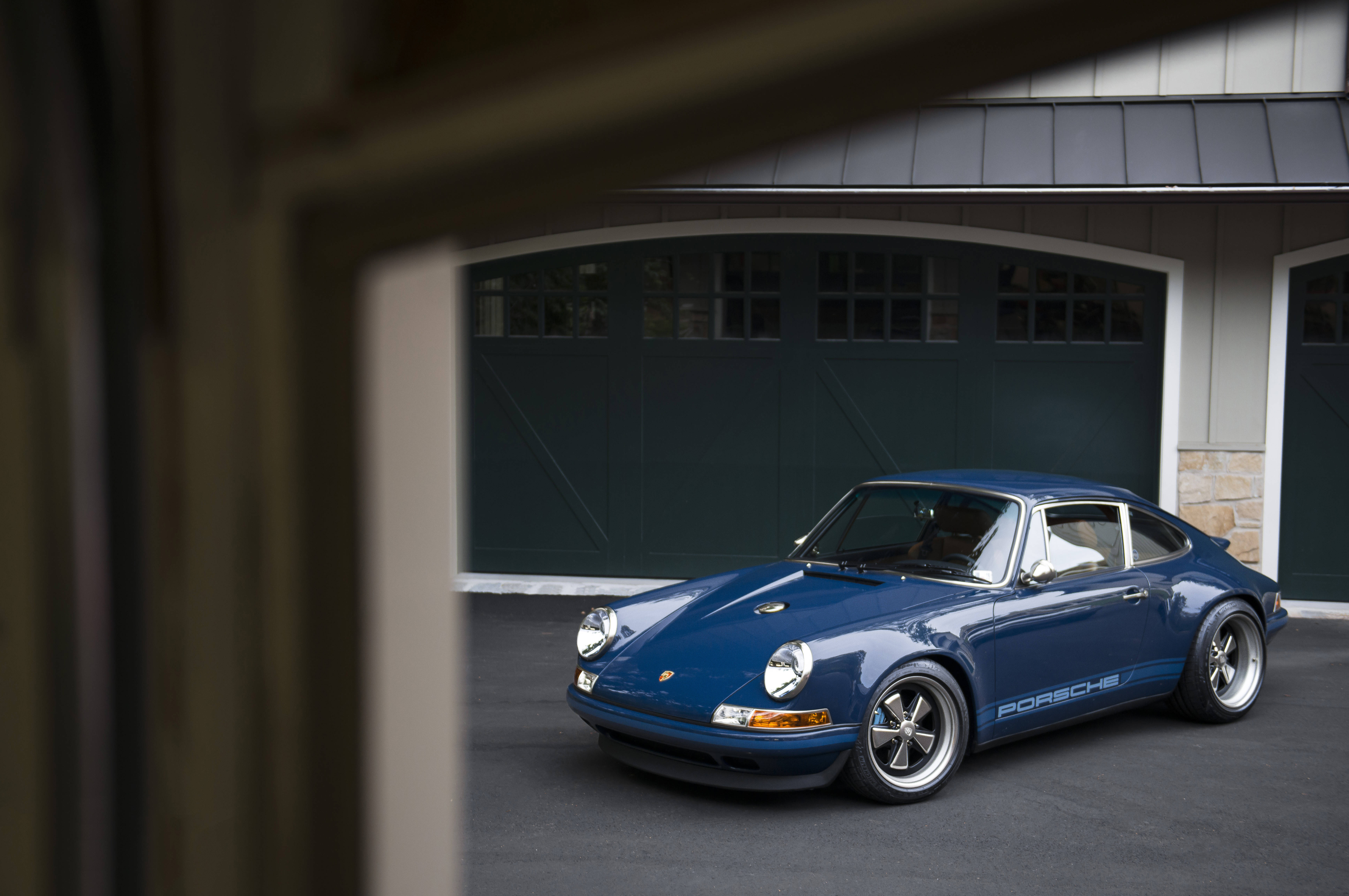 Singer 桌布 壁紙 — 一架時尚的藍色保時捷911經典跑車停放在現代車庫前，車庫有深綠色門。