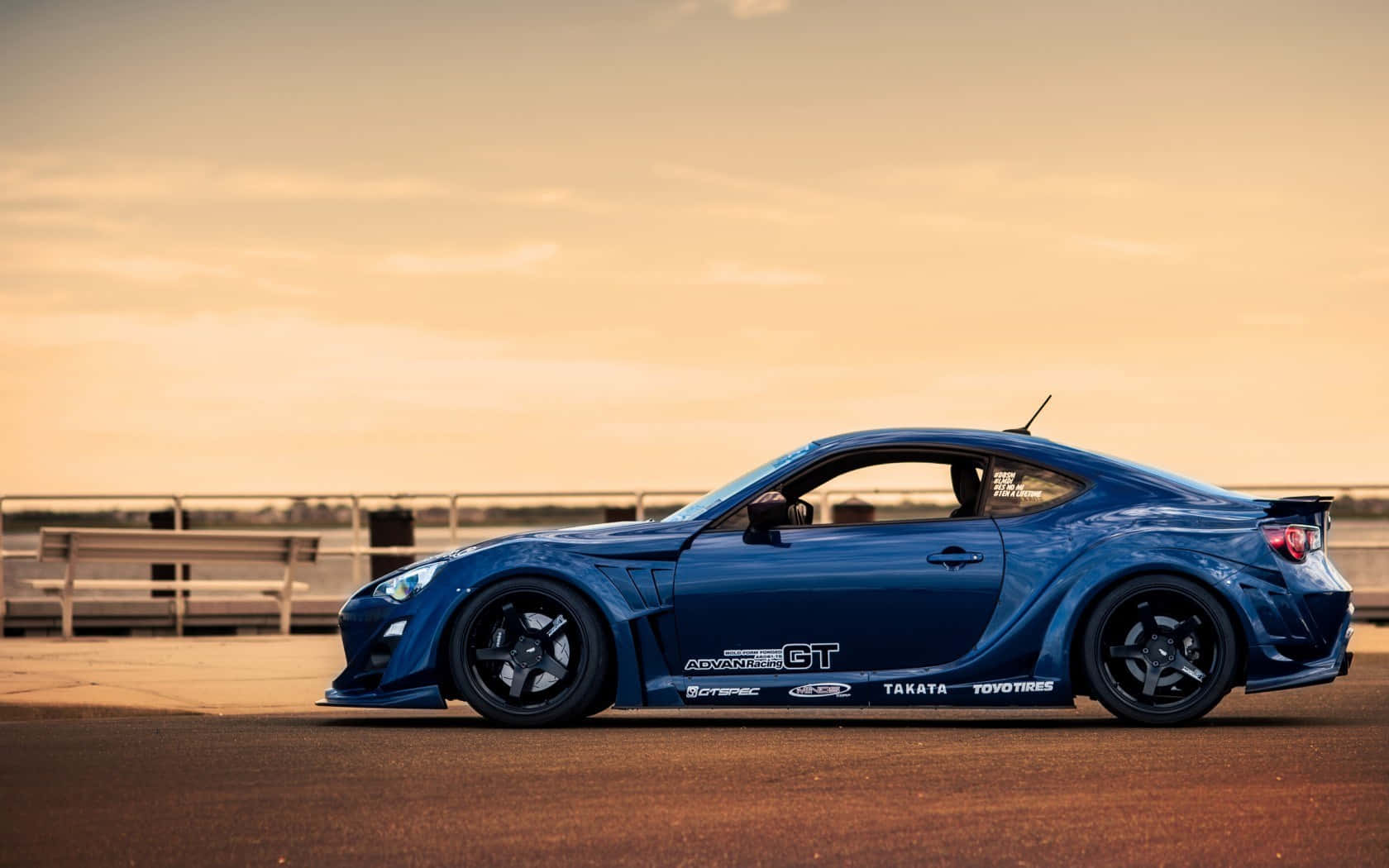藍色改裝跑車配備贊助商貼紙，在日落時停在瀝青路上。 — Toyota Supra Mk4 壁紙