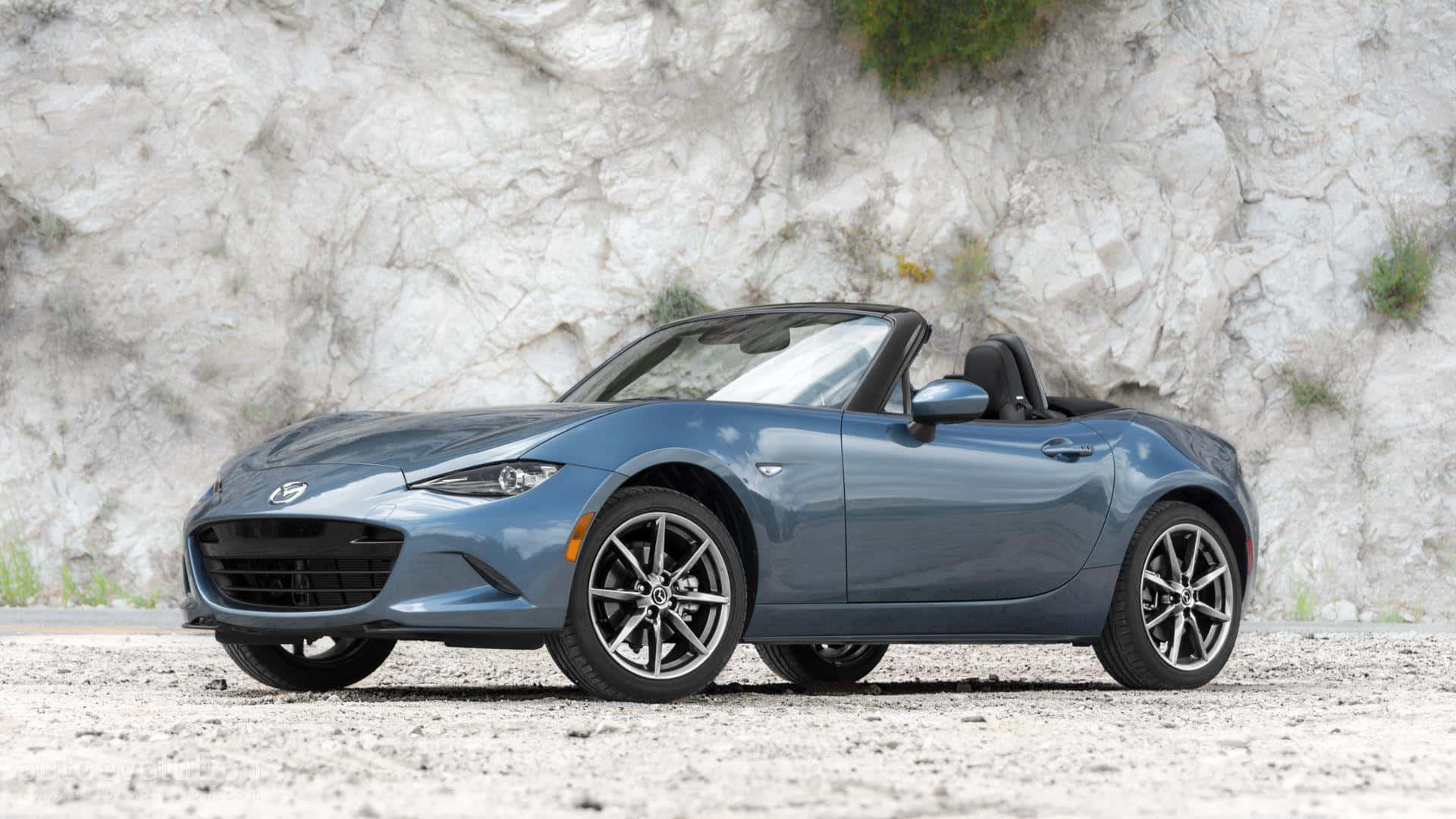 Miata 桌布 壁紙 — 一架時尚的藍色敞篷跑車停泊在碎石上，前面是紋理豐富的白色懸崖面。