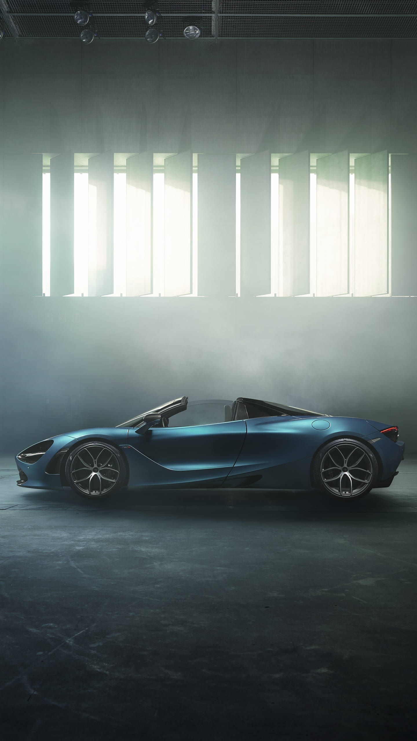 Mclaren 720s 桌布 壁紙 — 一架時尚的藍色敞篷跑車在煙霧瀰漫的工業倉庫中，在戲劇性的垂直光束下閃耀。