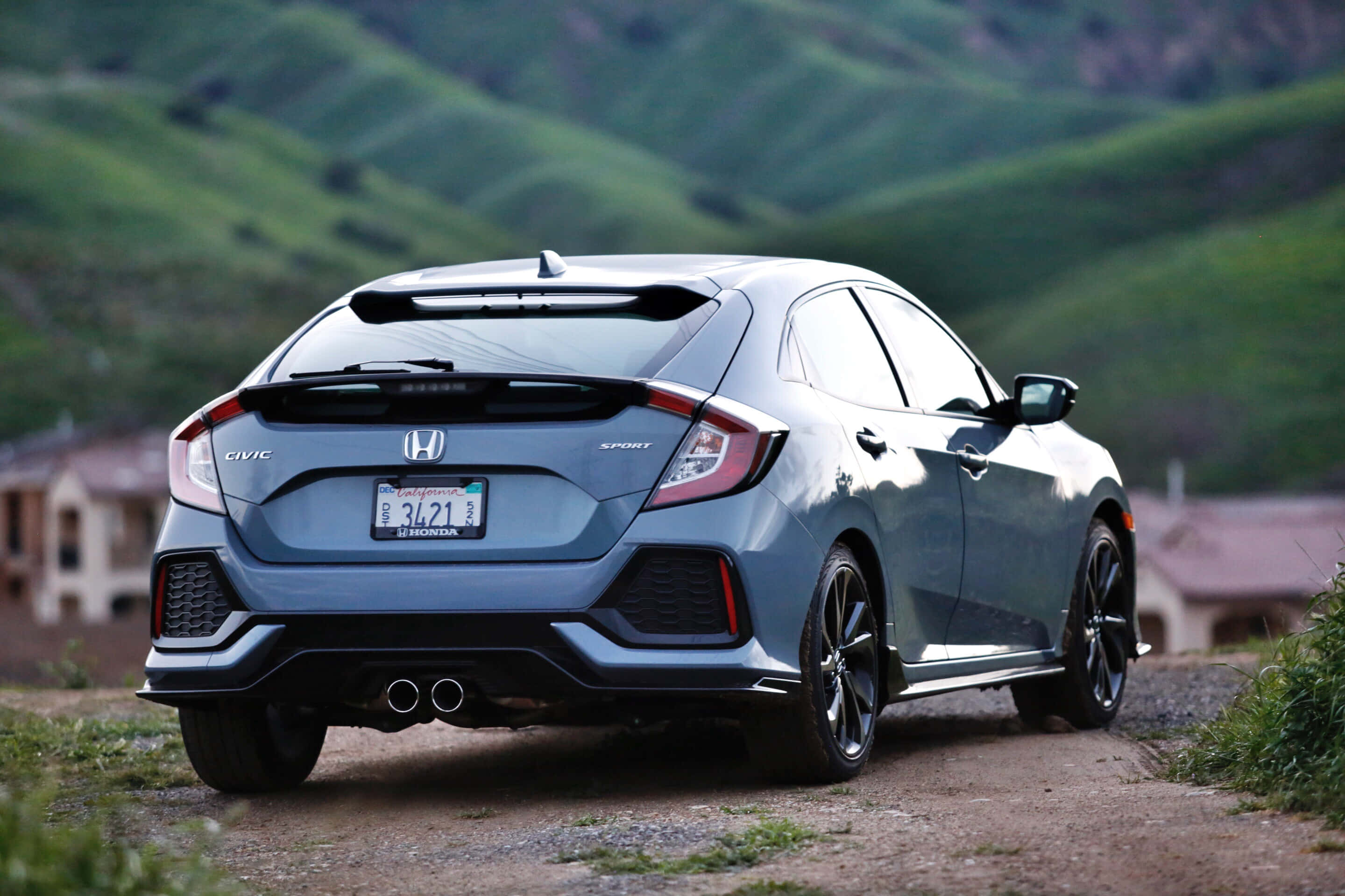 Honda Civic 桌布 壁紙 — 一架時尚的藍色本田Civic Sport停泊在泥路上，背景是起伏的綠色山丘。
