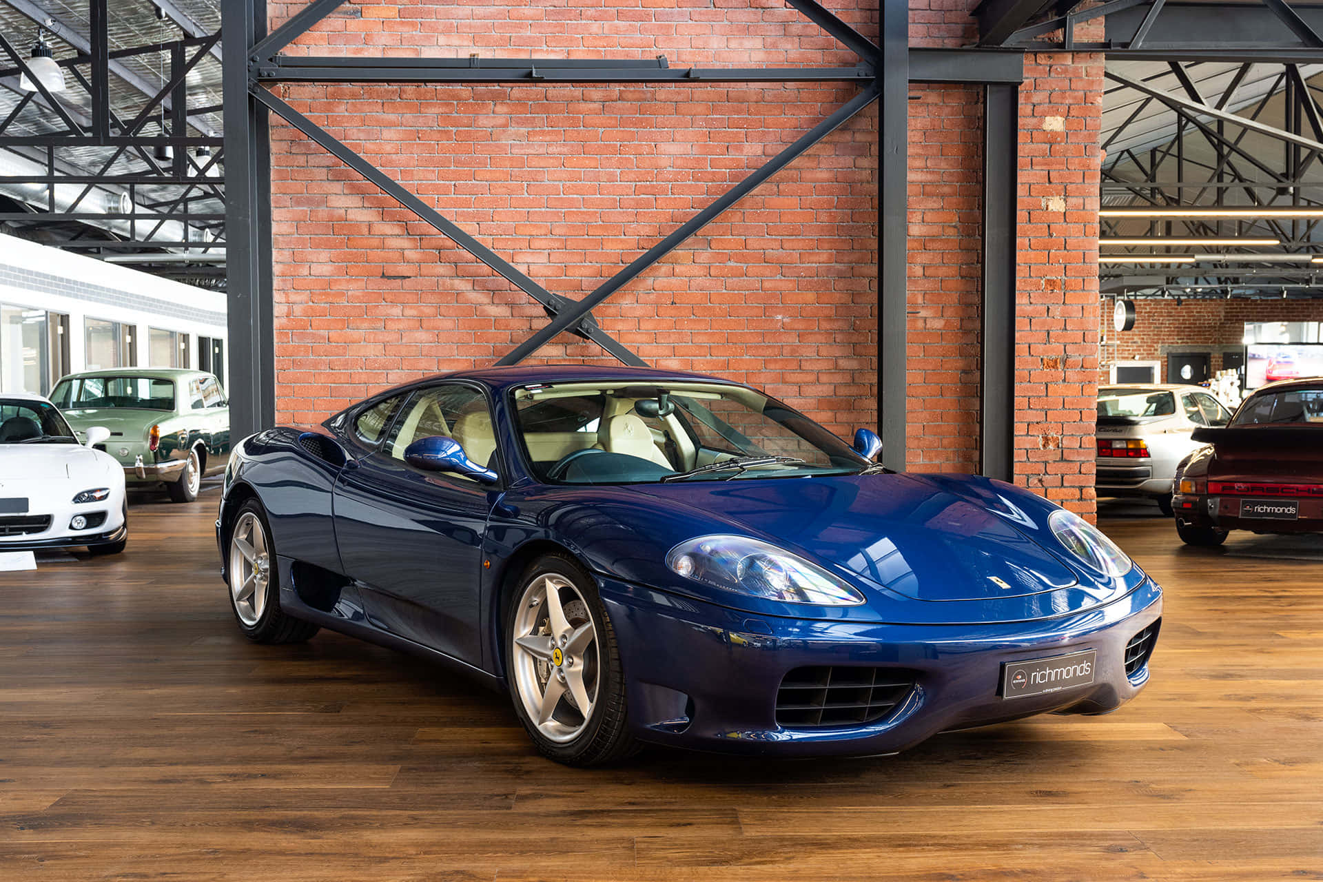 Ferrari 360 Modena 桌布 壁紙 — 一架時尚的藍色法拉利360跑車在帶有木地板的質樸磚牆車庫內，在明亮的燈光下閃閃發光。