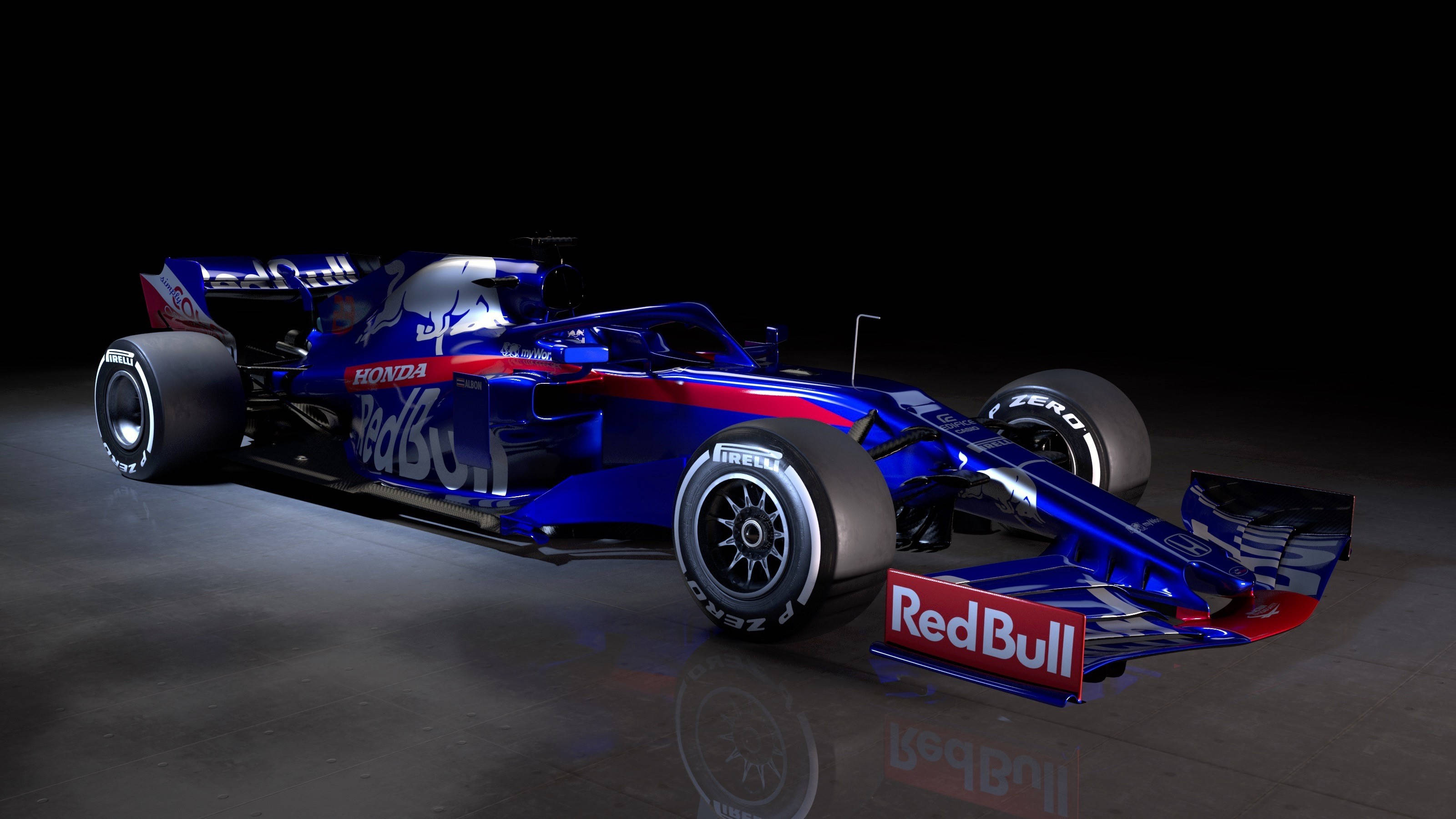 Formula One 桌布 壁紙 — 一架時尚的藍色紅牛一級方程式賽車，帶有紅色點綴和本田品牌標誌，在黑色背景的反射地板上被戲劇性地照亮。