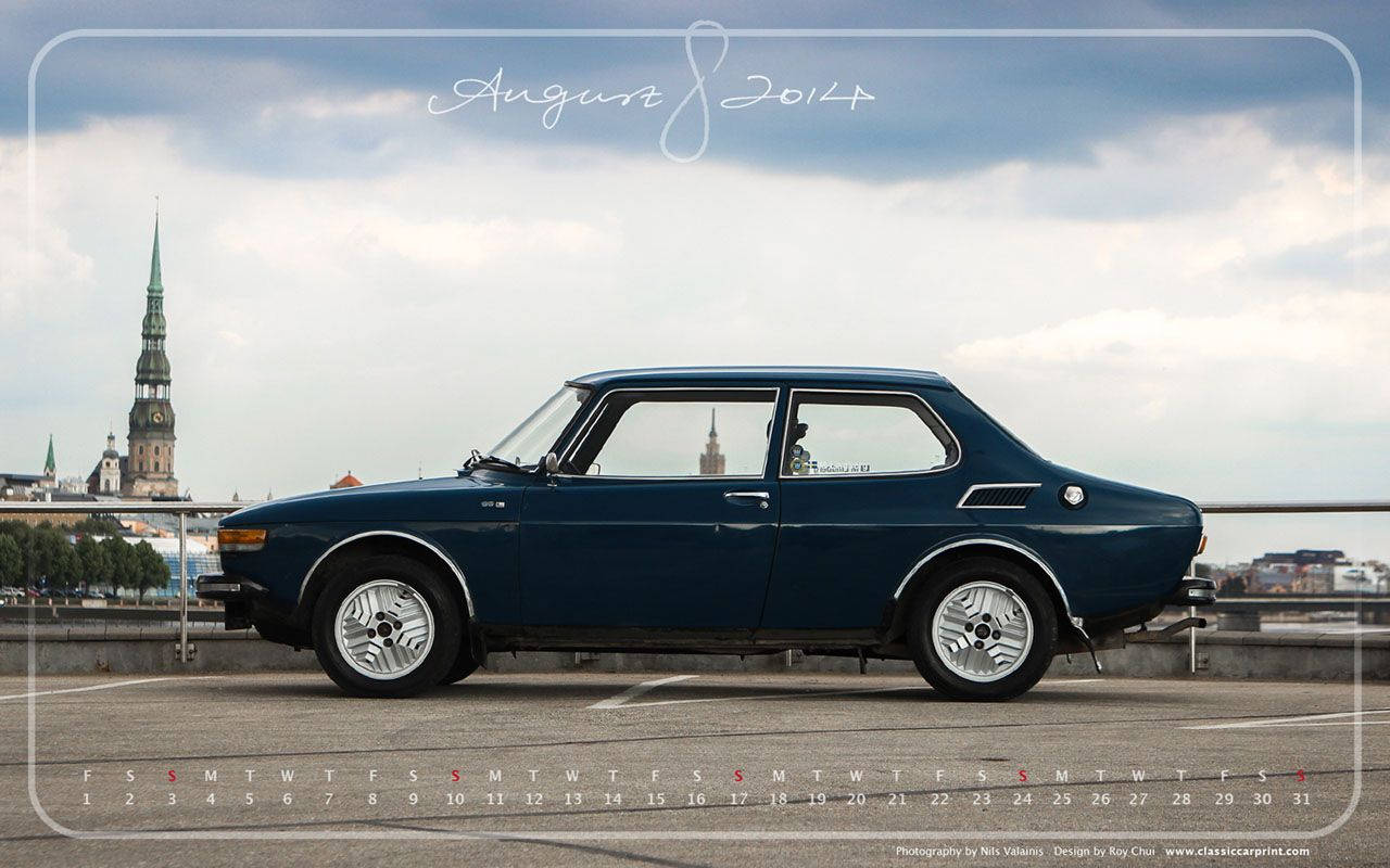 Saab 桌布 壁紙 — 一架時尚的藍色經典汽車停在一座橋上，背景是歷史悠久的城市天際線和教堂尖塔，天空多雲。