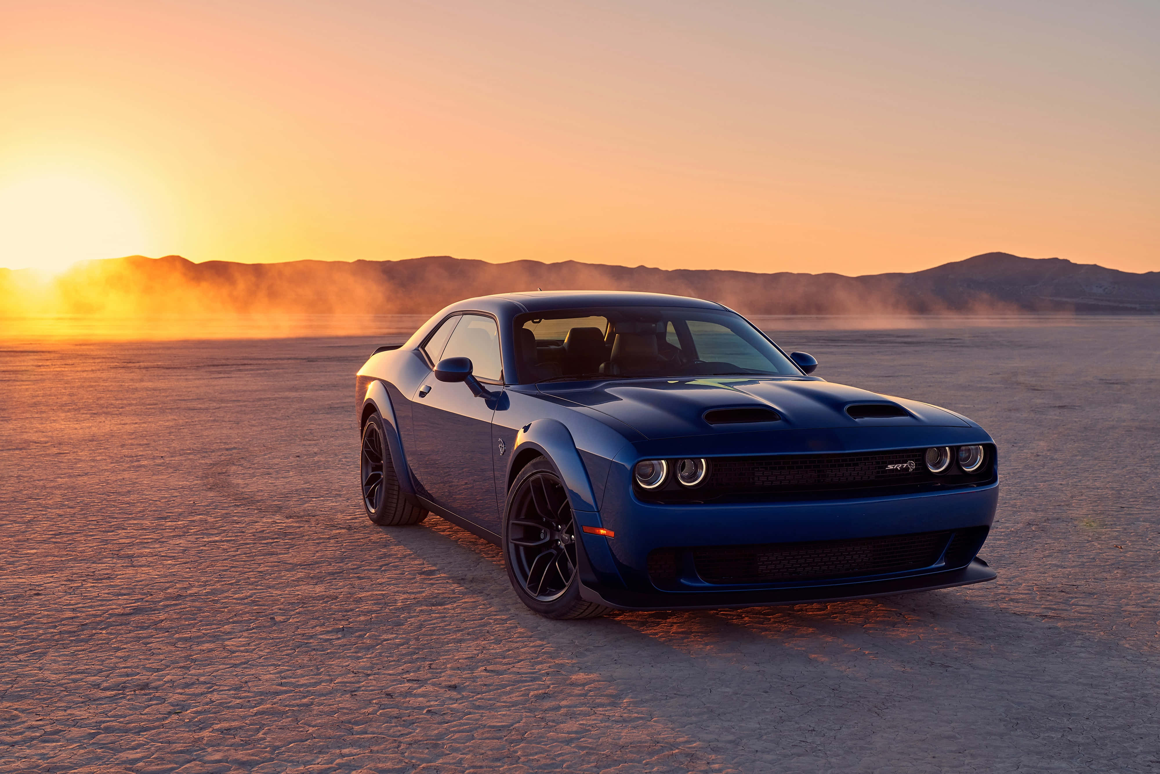 Dodge 桌布 壁紙 — 一架時尚的藍色肌肉車在金色日落時分，在廣闊的沙漠平原上揚起塵土。