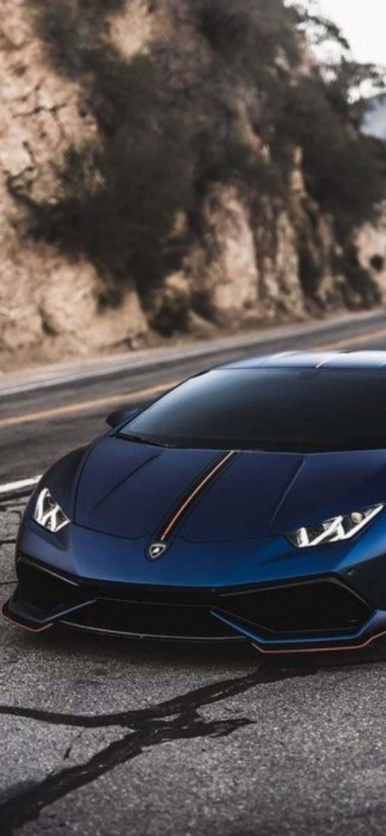 Lamborghini Phone 桌布 壁紙 — 一架時尚的藍色藍寶堅尼跑車停泊在蜿蜒的山路上，背景是岩石峭壁。