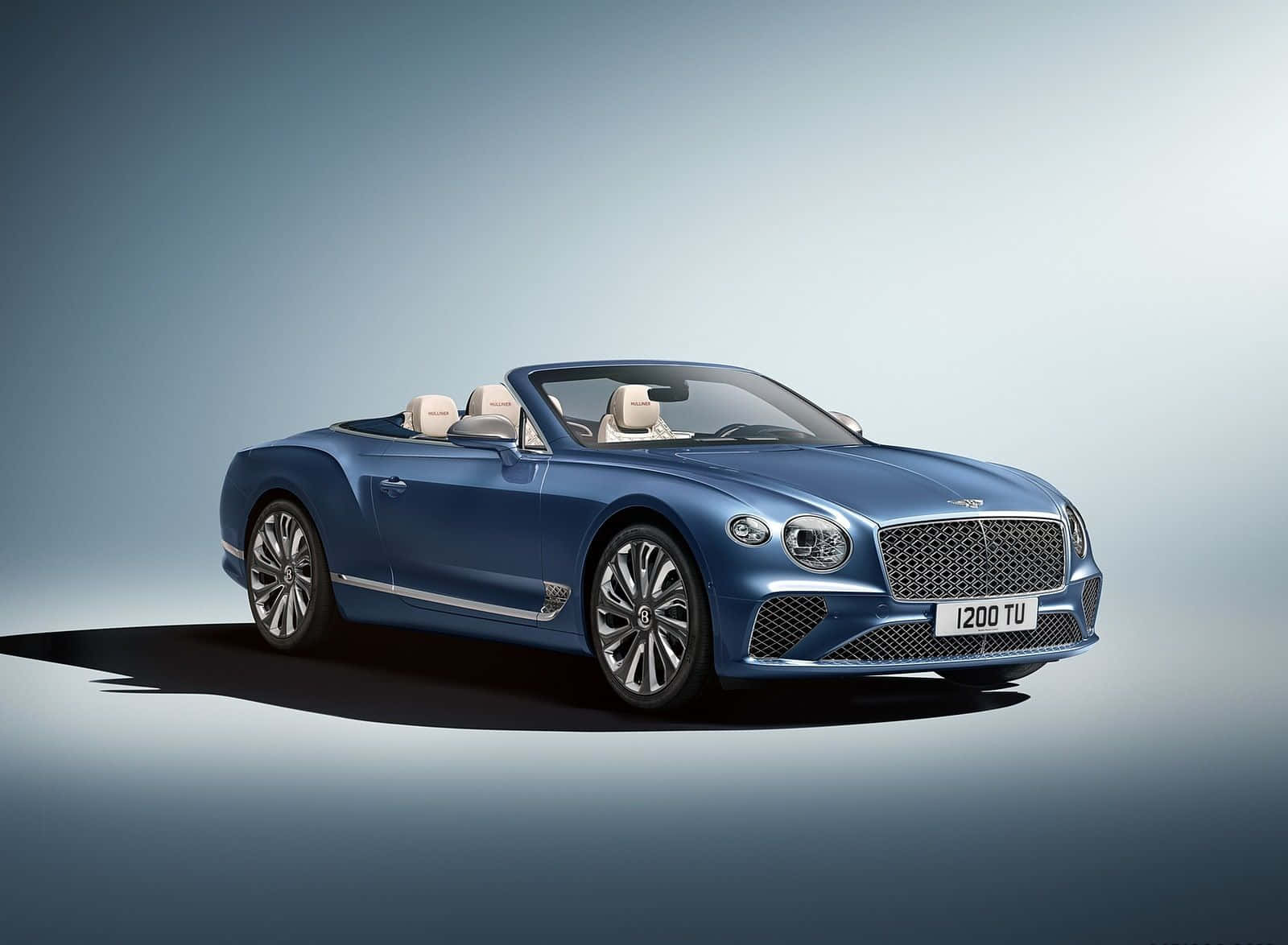 Best Bentley 桌布 壁紙 — 一架時尚的藍色賓利敞篷車搭配奶油色皮革座椅，在極簡漸變工作室背景前展示。