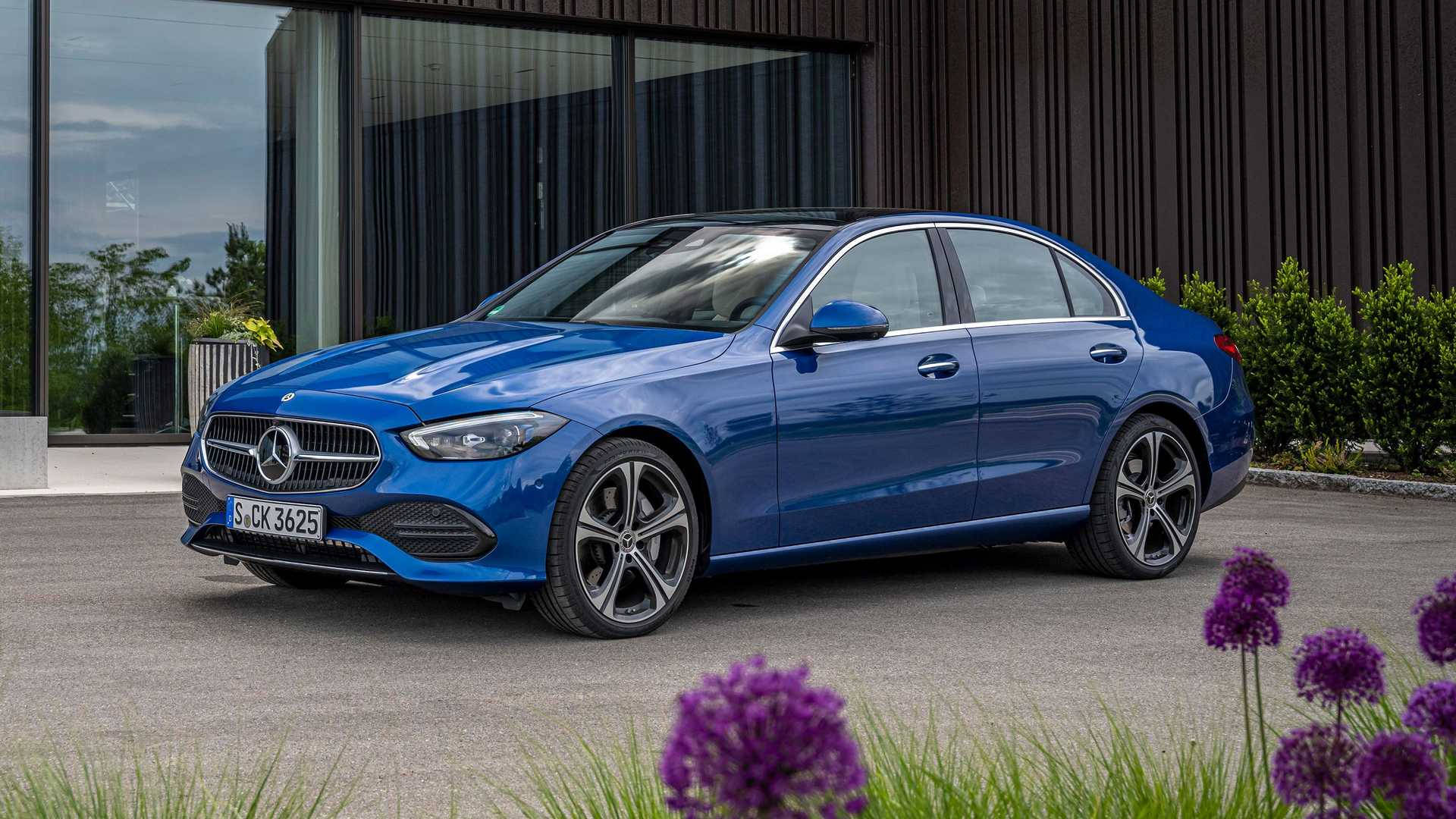 Mercedes Benz C300 桌布 壁紙 — 一架時尚的藍色賓士轎車停放在現代建築物前，前景有紫色花朵。