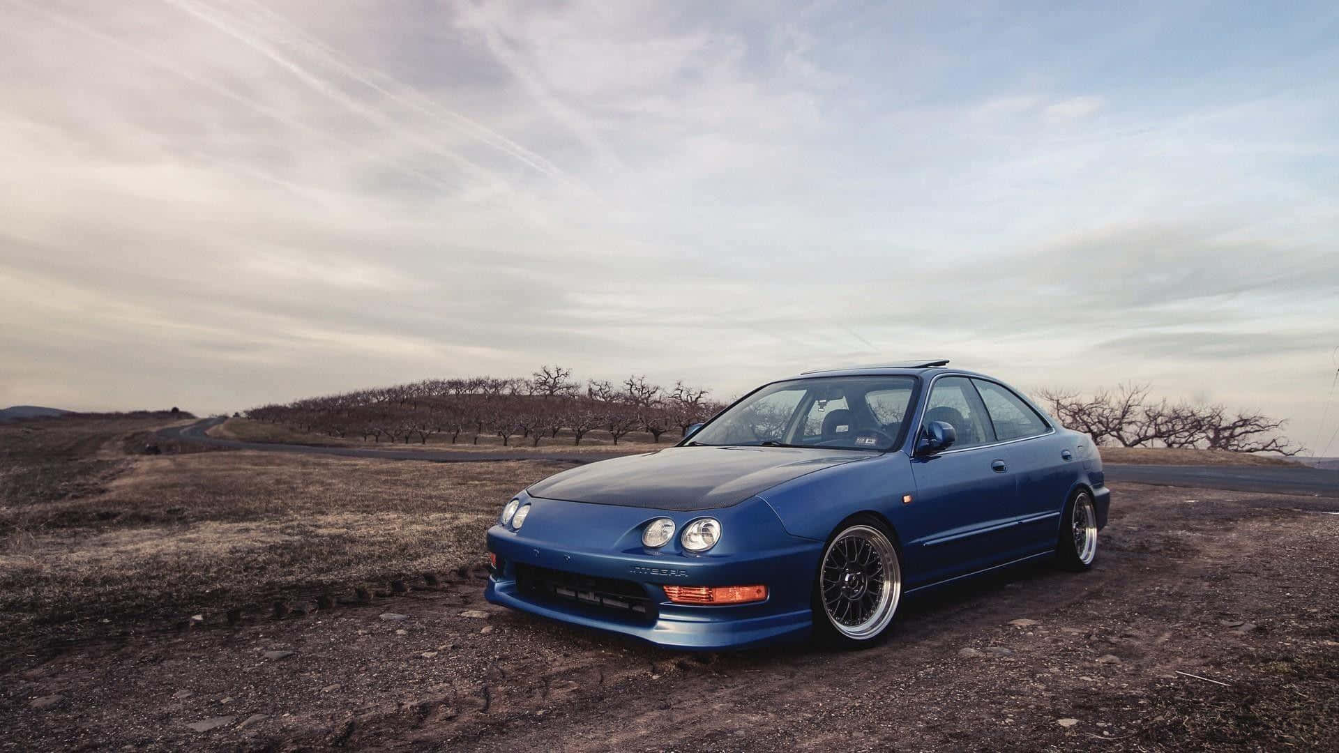Acura Integra 桌布 壁紙 — 一架時尚的藍色跑車停泊在多雲天空下的葡萄園旁邊的泥路上。