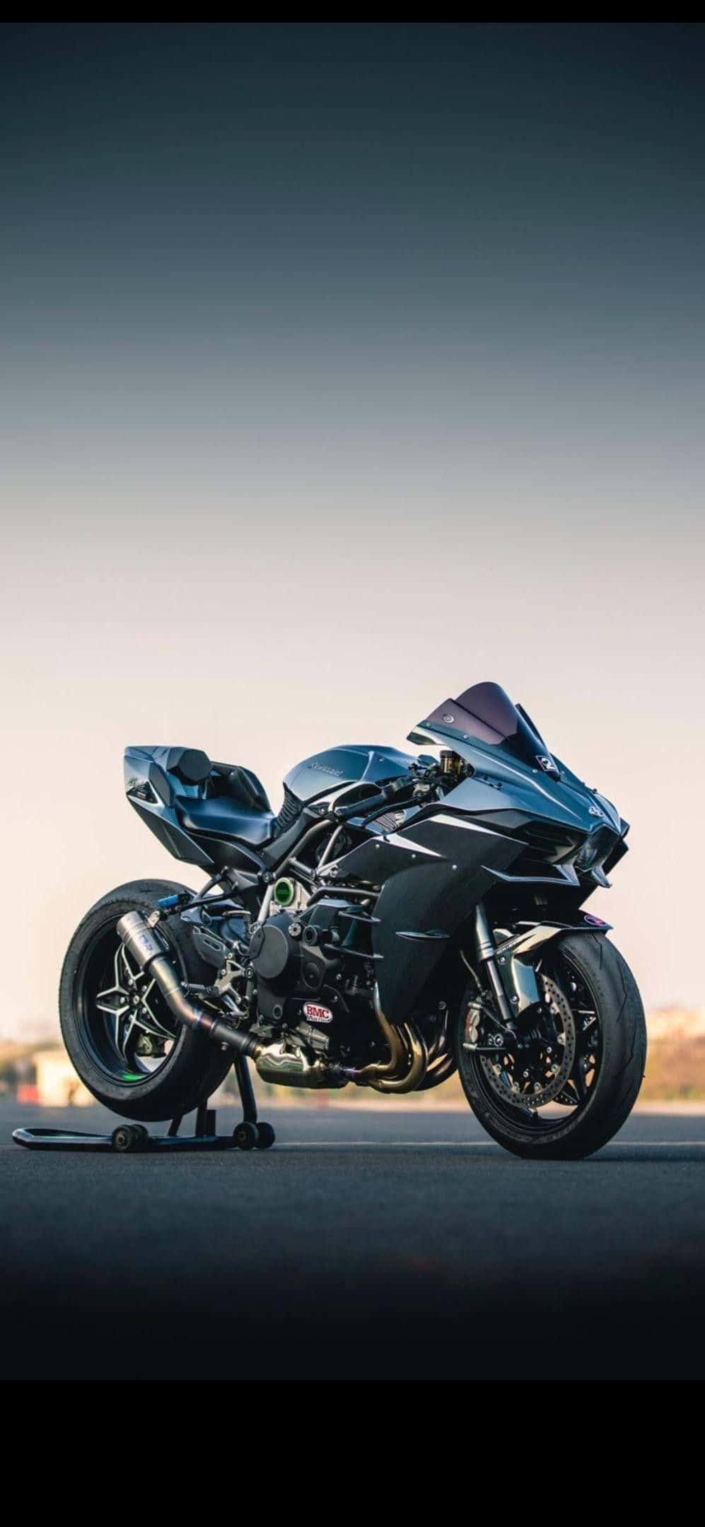 Motorcycle iPhone 桌布 壁紙 — 一架時尚的藍色運動機車在暮色中，停放在支架上，背景是漸變色的天空。