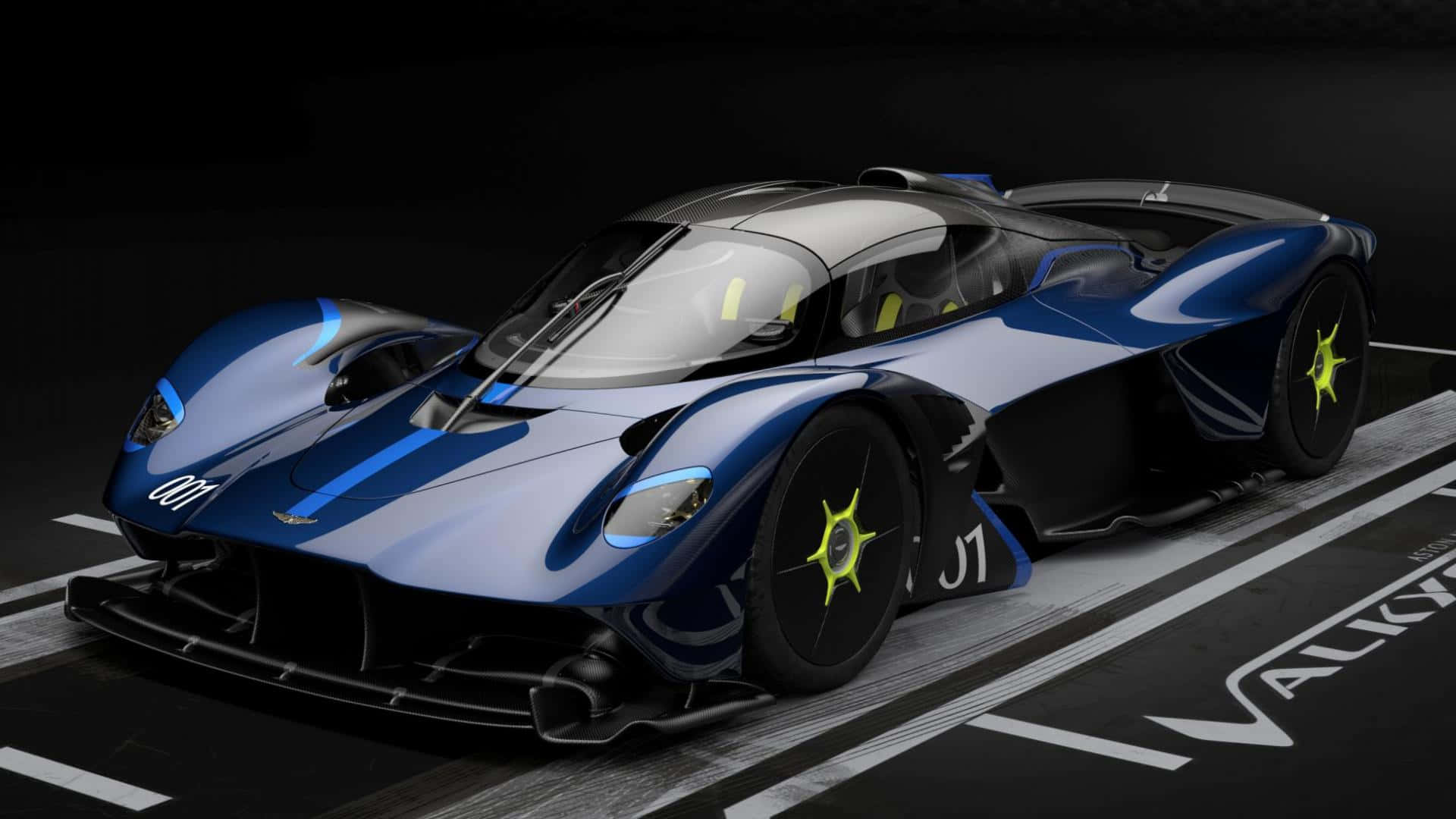 Aston Martin Valkyrie 桌布 壁紙 — 一架時尚的藍黑配色 Aston Martin Valkyrie 超跑，配備螢光黃色車輪，停放在印有其名字的賽道上。
