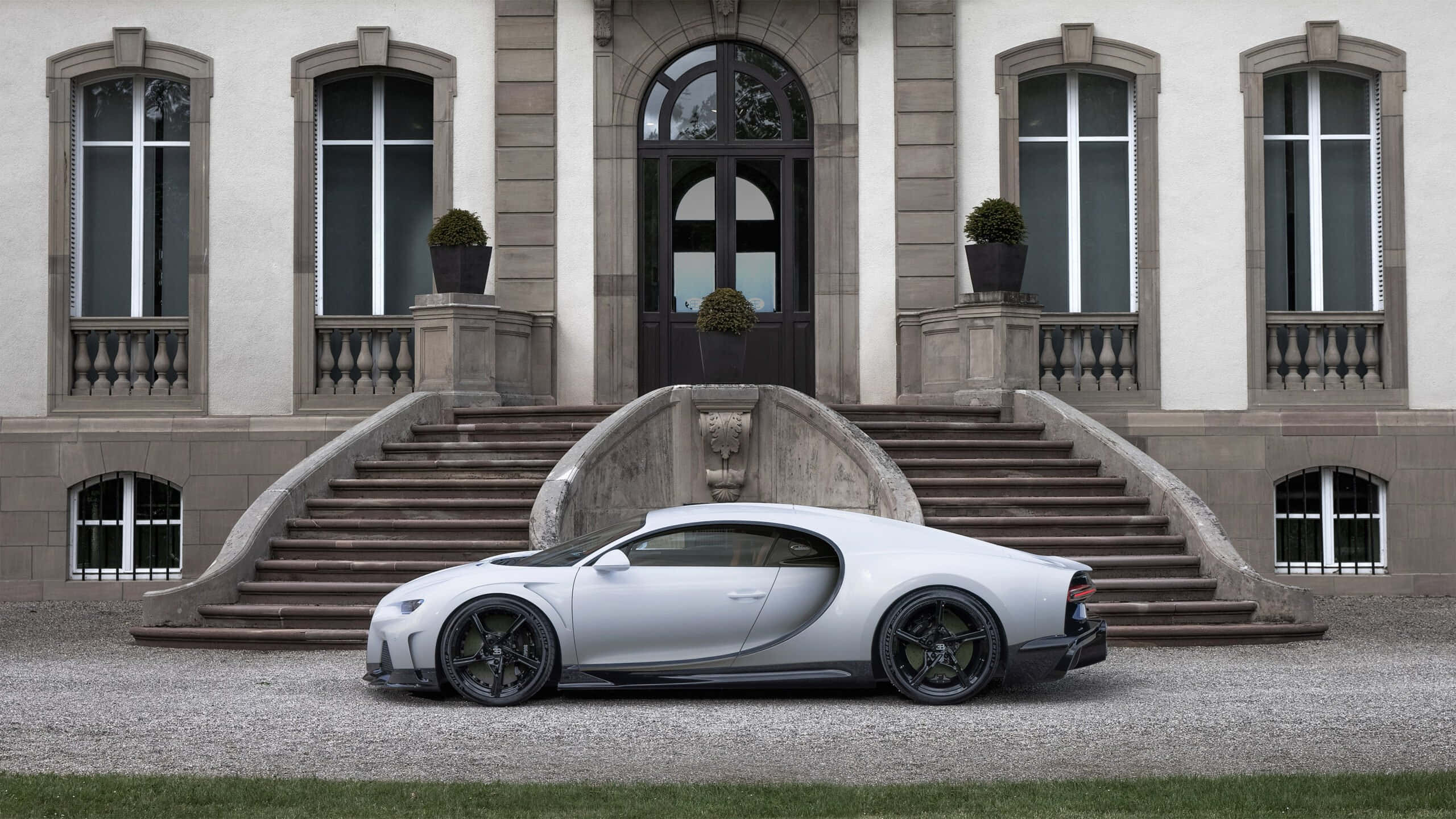 布加迪 桌布 壁紙 — 一架時尚的銀色 Bugatti Chiron 停泊在碎石路上，前方是一座宏偉的石砌大宅，配有拱形窗戶和對稱樓梯。