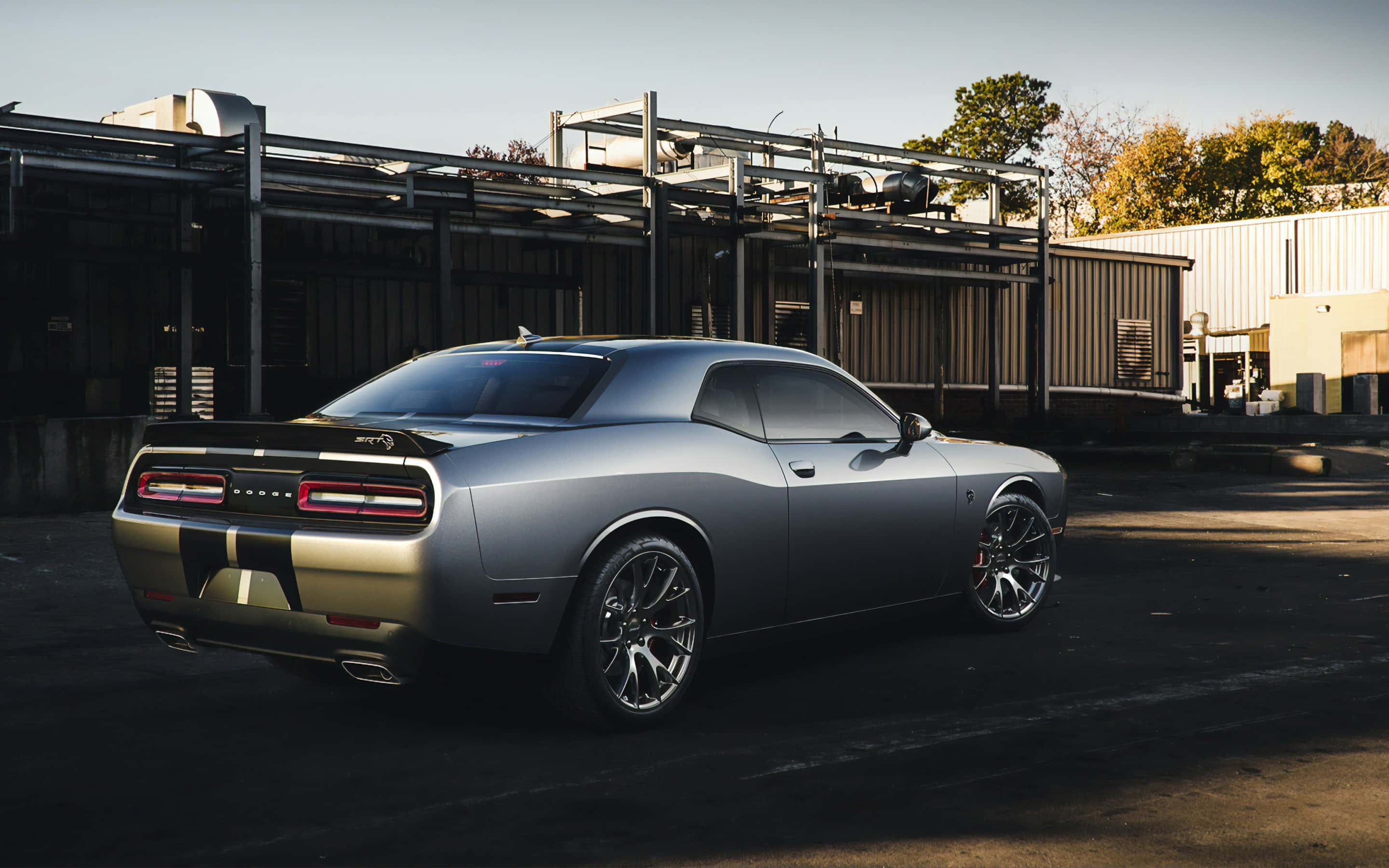 Hellcat 桌布 壁紙 — 一架時尚的銀色 Dodge Challenger 肌肉車停放在工業區，沐浴在金色的夕陽光中。